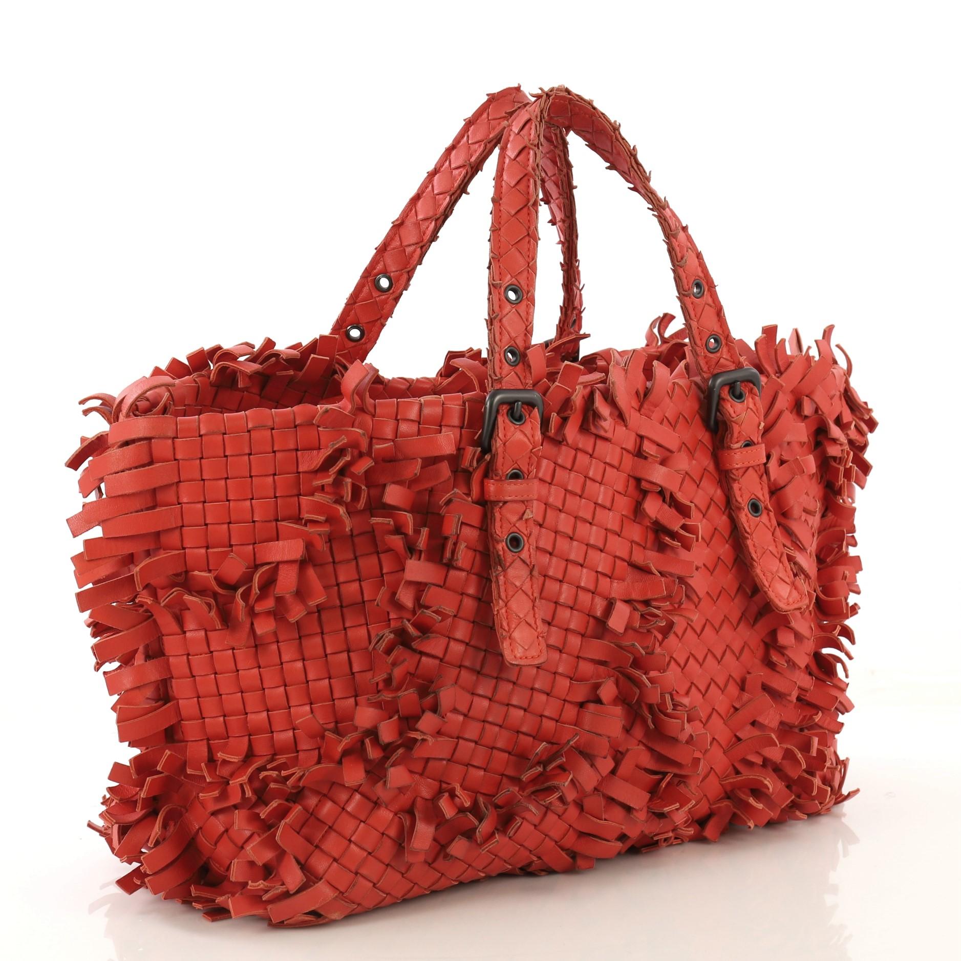 This Bottega Veneta Lido Patchwork Tote Fringe Intrecciato Nappa Large, crafted in red fringe intrecciato nappa leather, features dual handles with buckle and belt accents, patchwork and frayed fringed detailing, and gunmetal-tone hardware. It opens