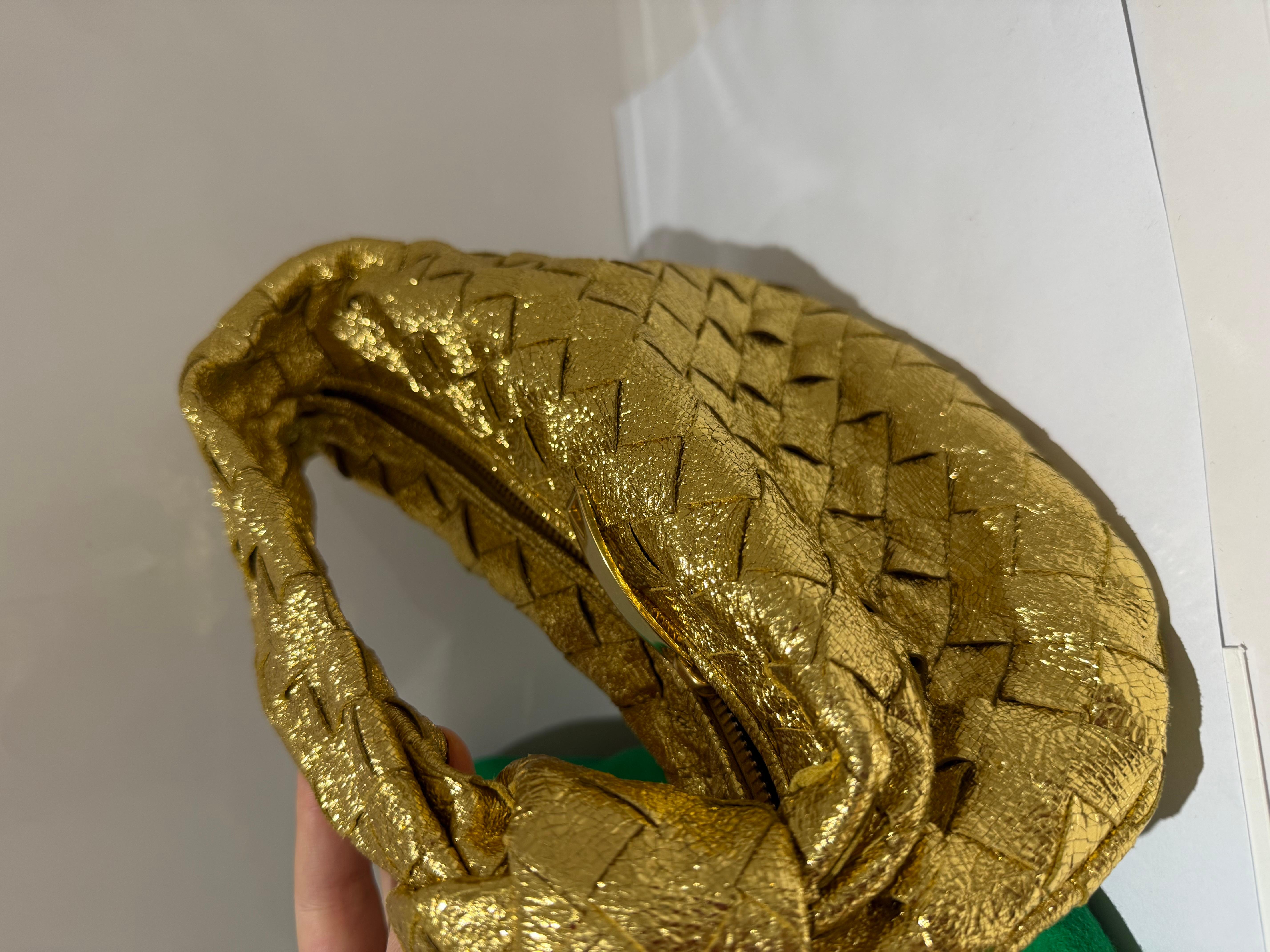 Mini sac Jodie de BOTTEGA VENETA en cuir Intrecciato métallisé or craquelé. Modèle en édition limitée.

Exclusivité Ramadan
• Mini sac à main en cuir métallisé intrecciato
• Compartiment unique
• fermeture éclair
100% cuir d'agneau
• Doublure : Peau