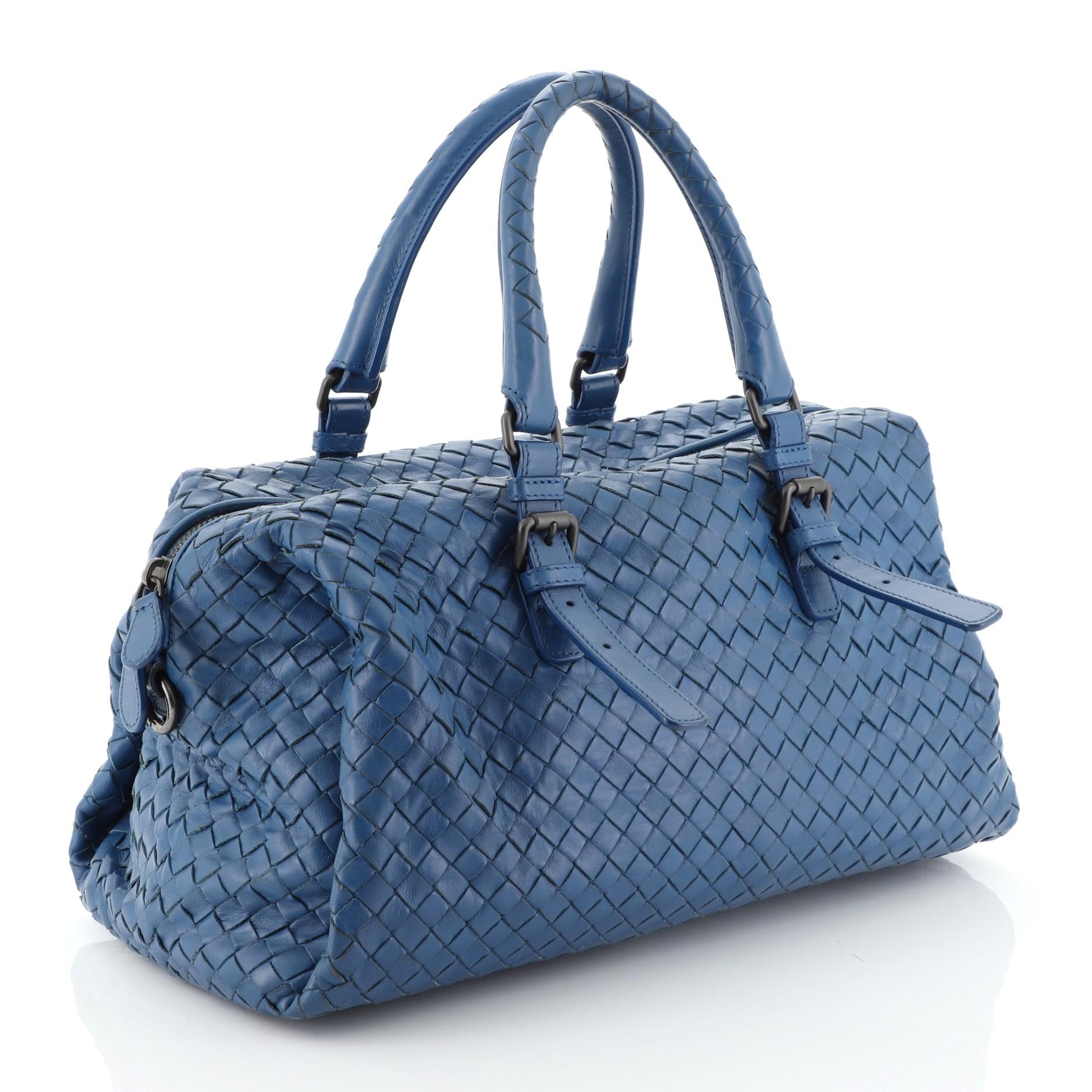 This Bottega Veneta New Boston Bag Intrecciato Nappa Medium, crafted from blue intrecciato nappa leather, features dual rolled handles with belt and buckle detailing and matte gunmetal-tone hardware. Its top zip closure opens to a neutral suede