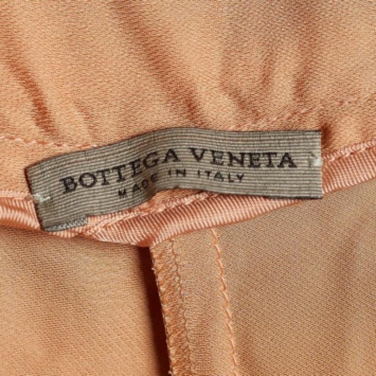 Estos pantalones de la Casa Bottega Veneta son todo lo que necesitas para presumir de lujo y comodidad. Están confeccionadas con tejido de satén naranja en una silueta de corte recto. Presentan un detalle de lazo en la cintura y dos bolsillos.