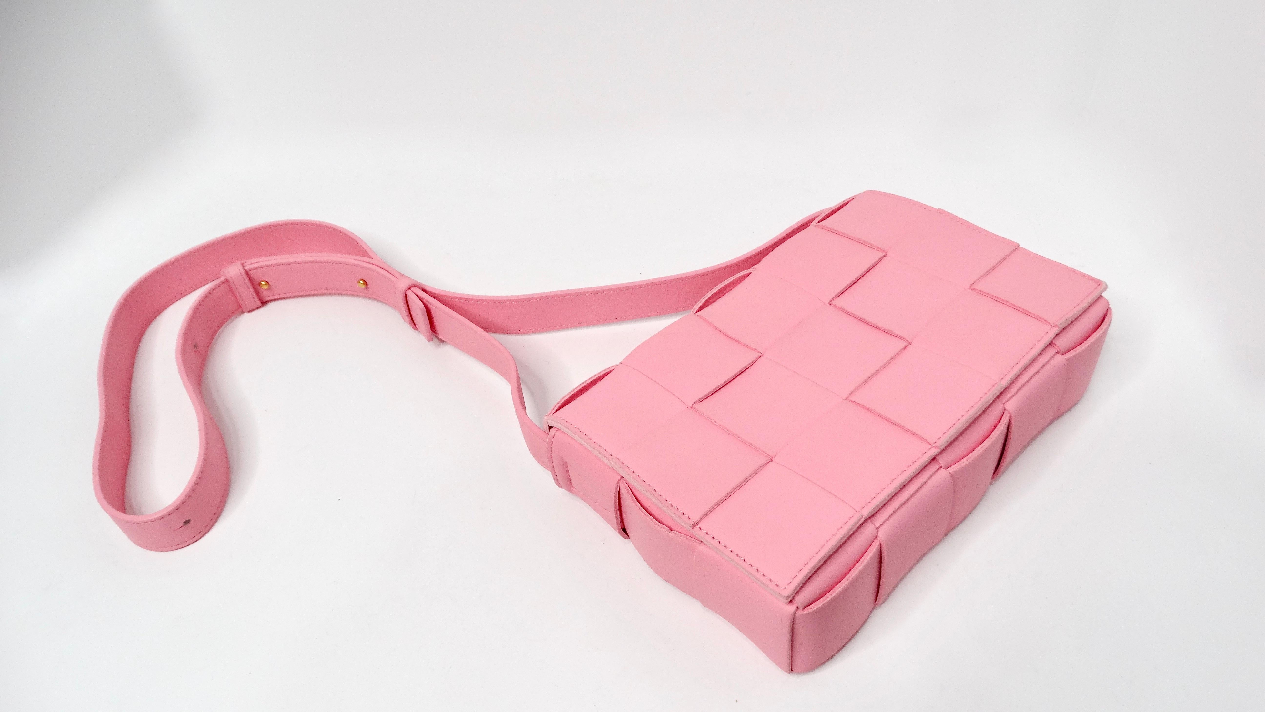 The Bottega Veneta Pink Cassette Leather Crossbody Bag is an exquisite blend of playful elegance and contemporary design. Crafted from soft bubblegum pink leather, this messenger-style bag stands out with its signature padded weave, showcasing the