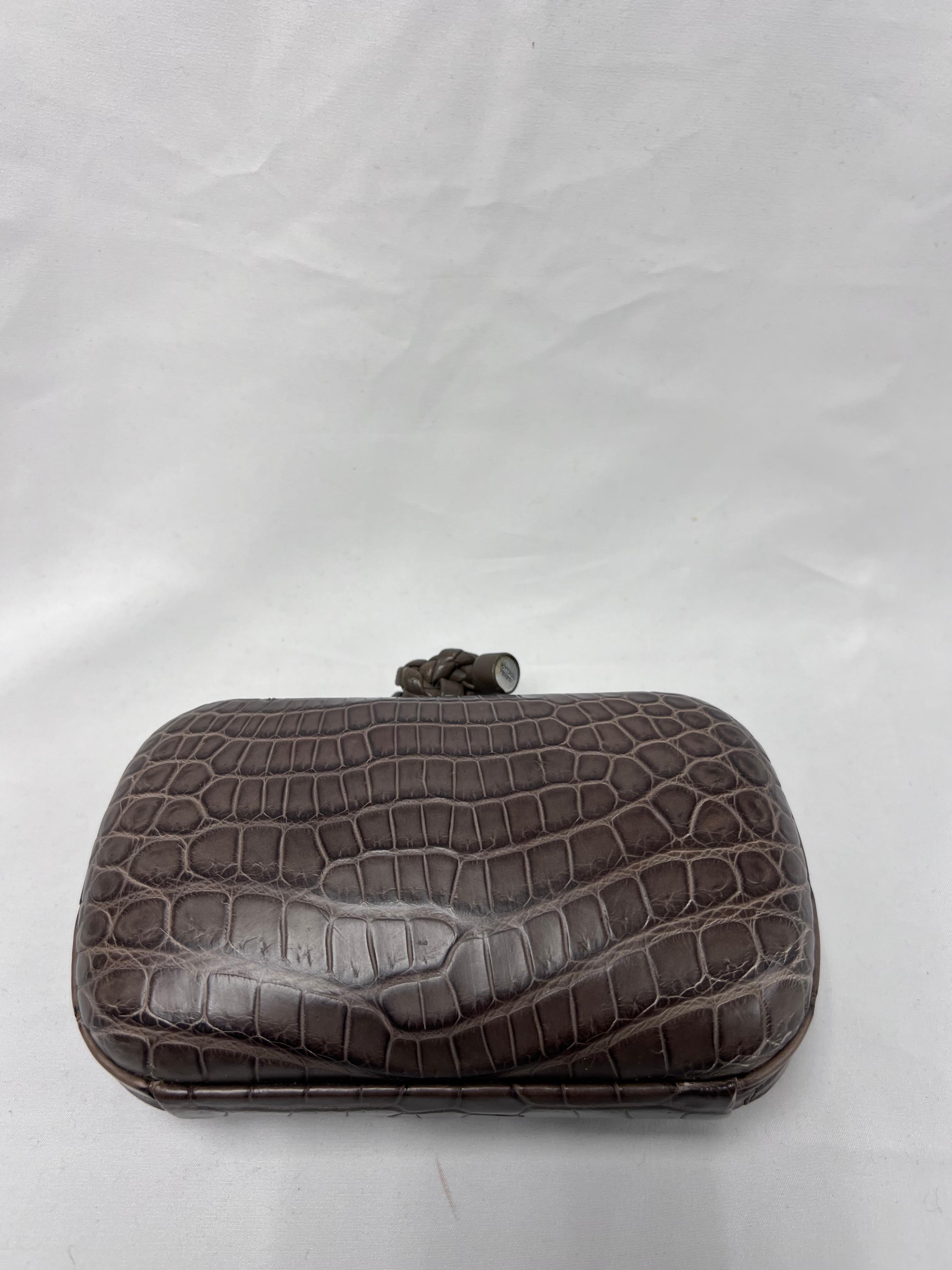 This is an authentic BOTTEGA VENETA Crocodile Knot Clutch in Brown. This stylish clutch is crafted of brown crocodile and a knot lock. This lock opens to a beige suede interior.

Dimensions: 7 in L x 4.5 in H x 1.75 in W (17.8 cm x 11.4 cm x 4.4