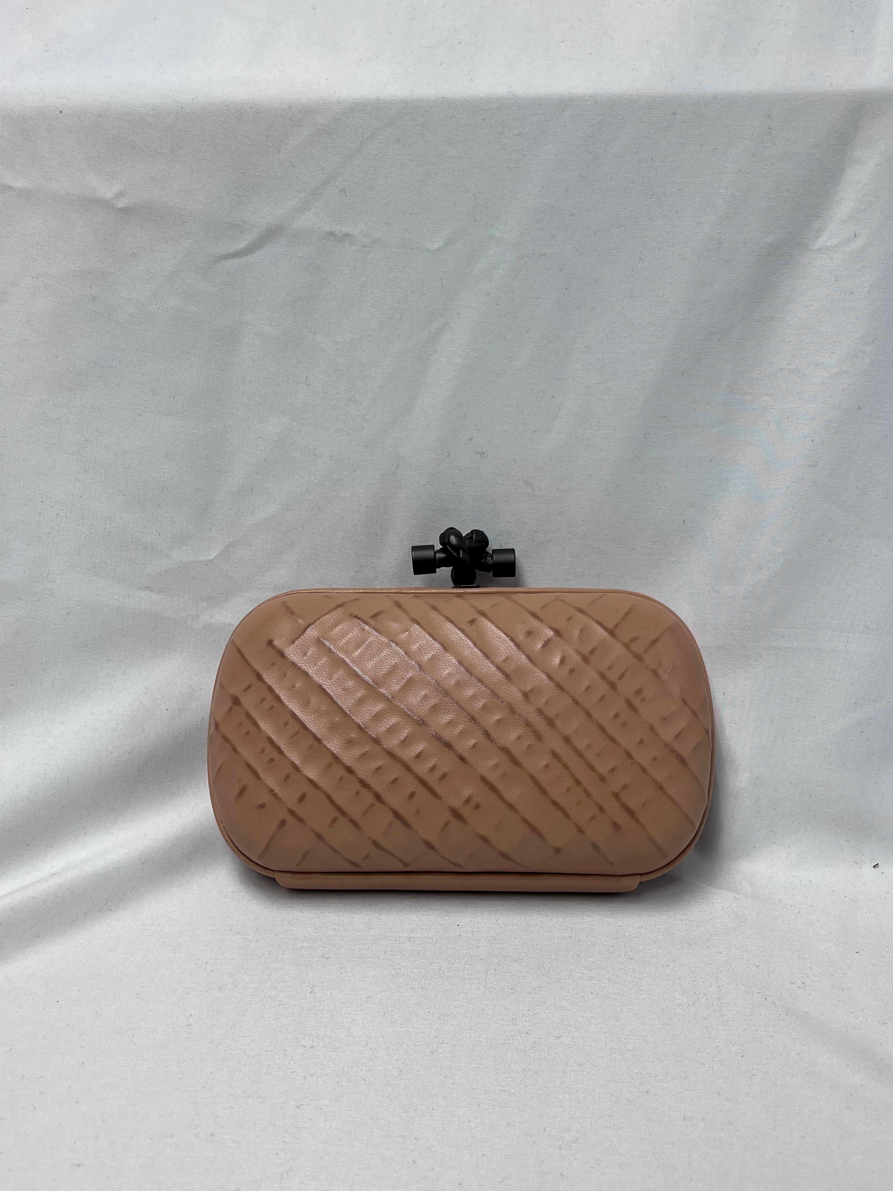 Introducing an authentic Bottega Nappa Embossed Knot Clutch in Light Brown. This elegant clutch, designed in a chic case style, is made from brown nappa leather with a distinctive woven texture. It showcases a knot-shaped kiss lock that reveals a