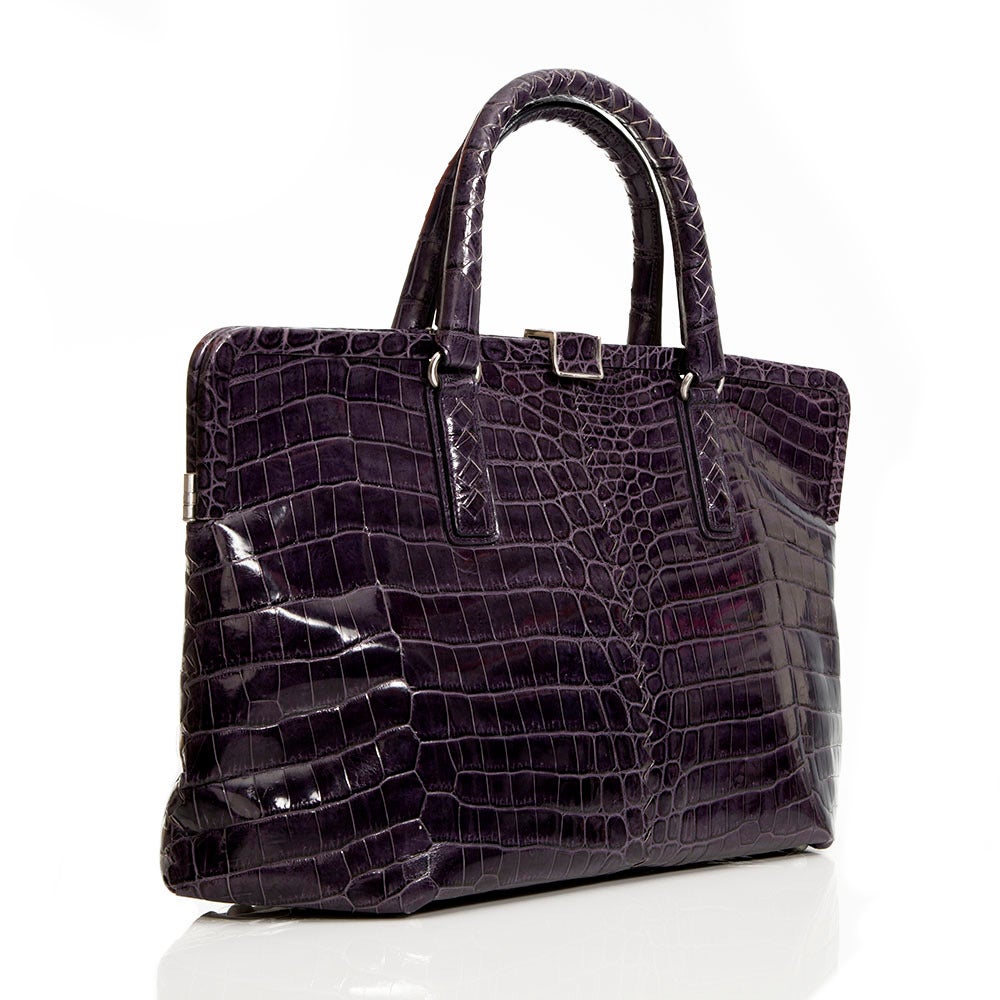 Featuring an exquisite exotic skin in eggplant purple, this handbag from Bottega Veneta is complimented by silver hardware on the handles and clasp and a hexagonal opening. This piece has a large interior along with an internal zip-compartment and