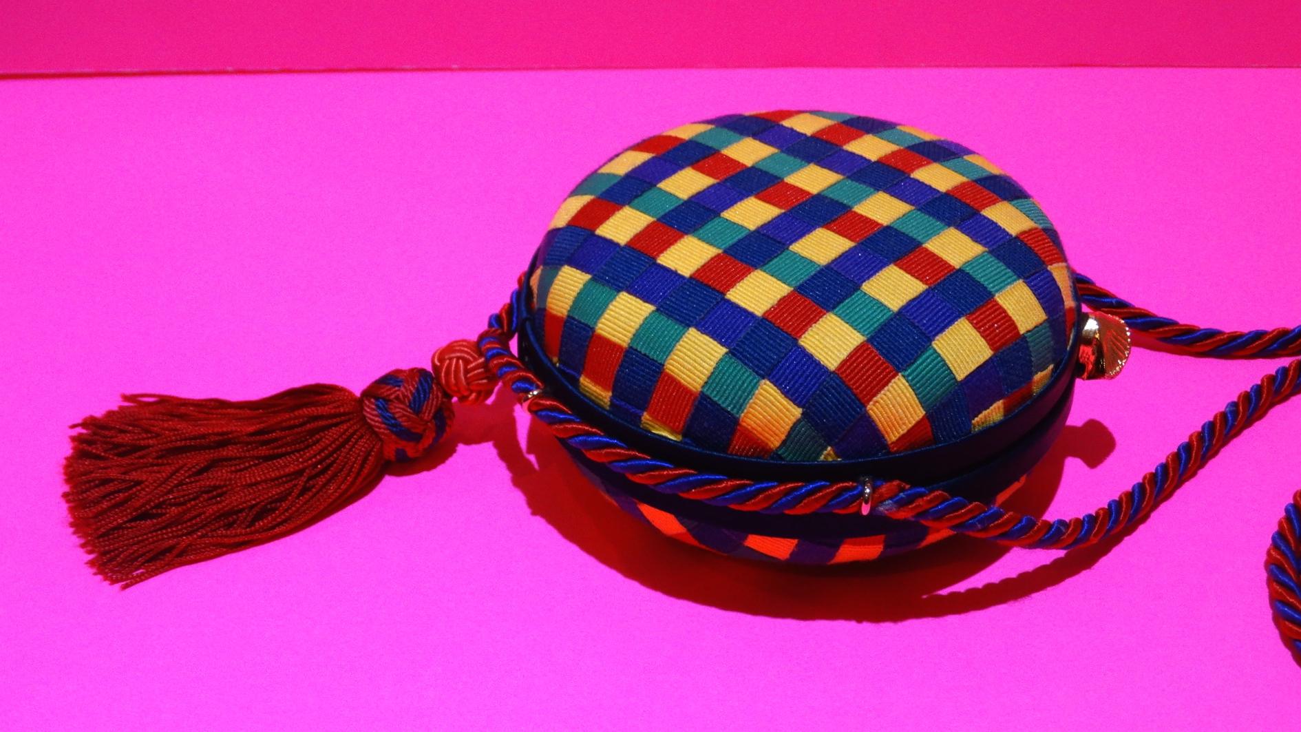 Your perfect little summer bag has arrived! Adorable 1980s plaid printed circular bag from designer Bottega Veneta! Printed all over in a rainbow gingham style plaid fabric with red and blue braided trim. Matching red and blue tassel suspended from