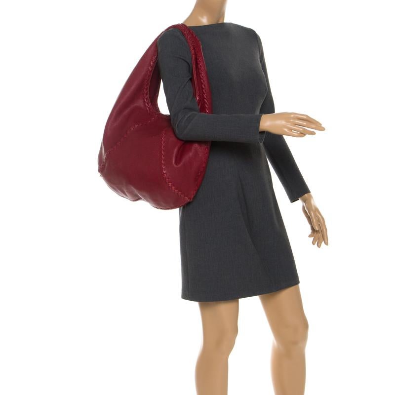 Crafted in Italy, this Bottega Veneta Baseball hobo is made of Cervo leather and comes in a striking shade of red. It has a classic silhouette and features a single handle. The exterior is beautified with woven leather trims and the spacious