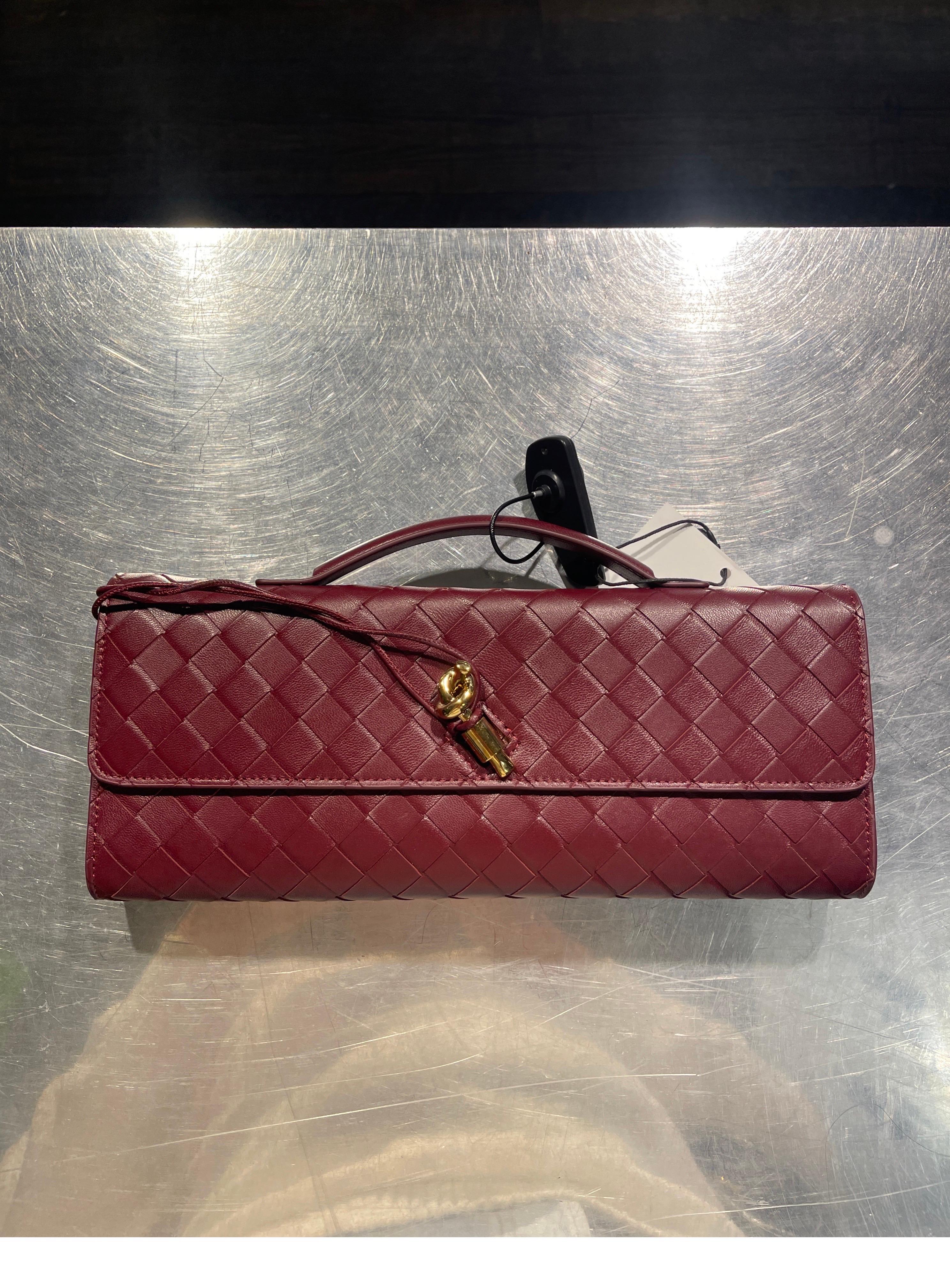 This is an authentic BOTTEGA VENETA Nappa Intrecciato Long Andiamo Top Handle Clutch in Burgundy. This stylish bag is crafted of Burgundy nappa leather. It features a leather top handle and a gold-tone knot detail at the front. The flap opens to a