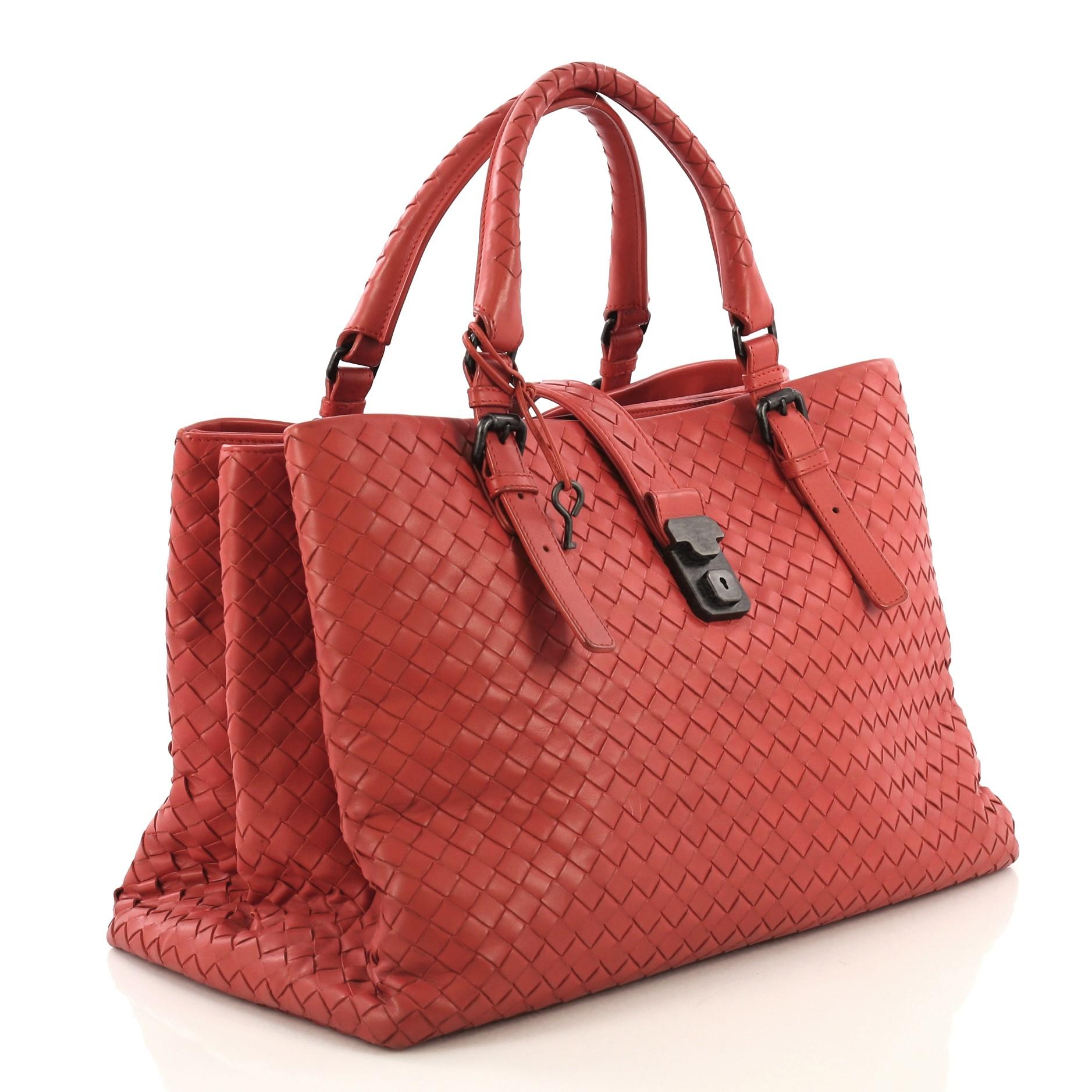 This Bottega Veneta Roma Handbag Intrecciato Nappa Medium, crafted in red intrecciato nappa leather, features dual woven leather handles with buckle detailing, push lock tab opening and matte gunmetal-tone hardware. It opens to taupe suede interior