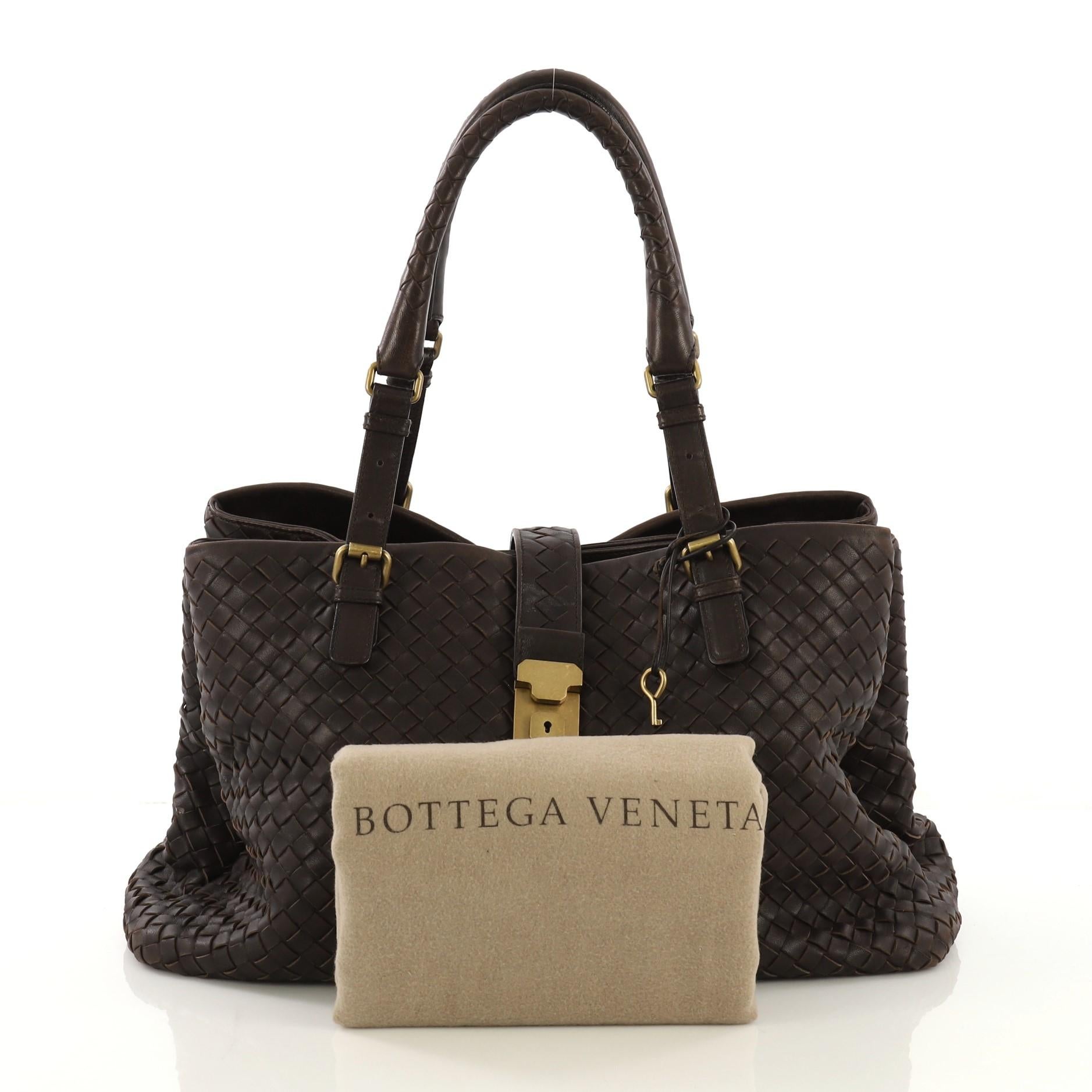 This Bottega Veneta Roma Handbag Intrecciato Nappa Medium, crafted in brown intrecciato nappa leather, features dual woven leather handles with buckle detailing, push lock tab opening and gold-tone hardware. It opens to beige suede interior divided