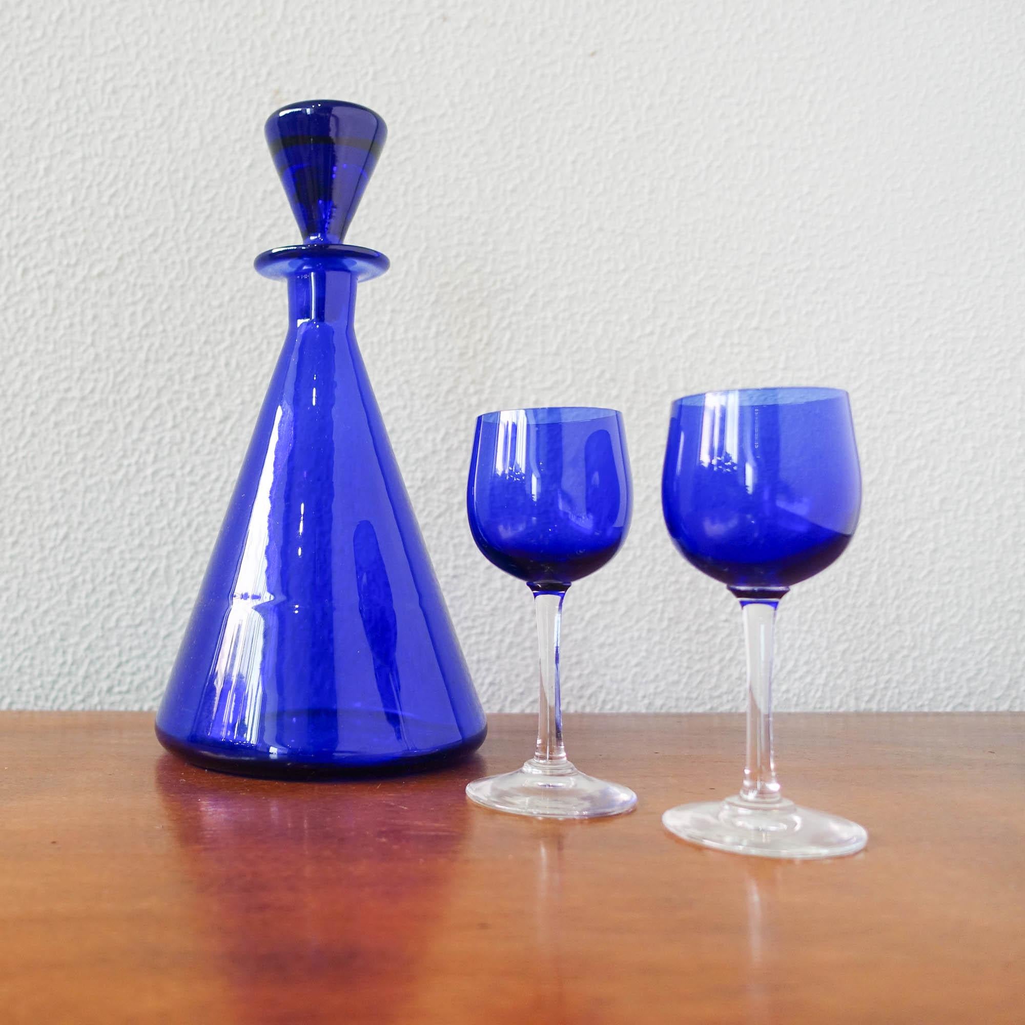Questo set di bottiglie e due bicchieri è stato progettato e prodotto da Marinha Grande, in Portogallo, negli anni Cinquanta. La bottiglia è interamente in vetro blu cobalto, mentre i bicchieri sono in blu cobalto con base e stelo trasparenti. In