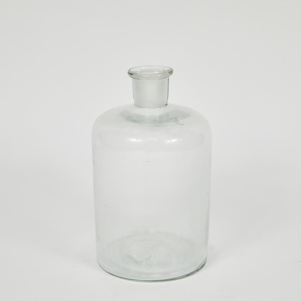 English mid-century clear glass bottles in graduated sizes with round matching glass stoppers. The bottles are satisfyingly heavy, with a beautiful rustic quality to the glass. They could work as vases or as a decorative addition to a cabinet or