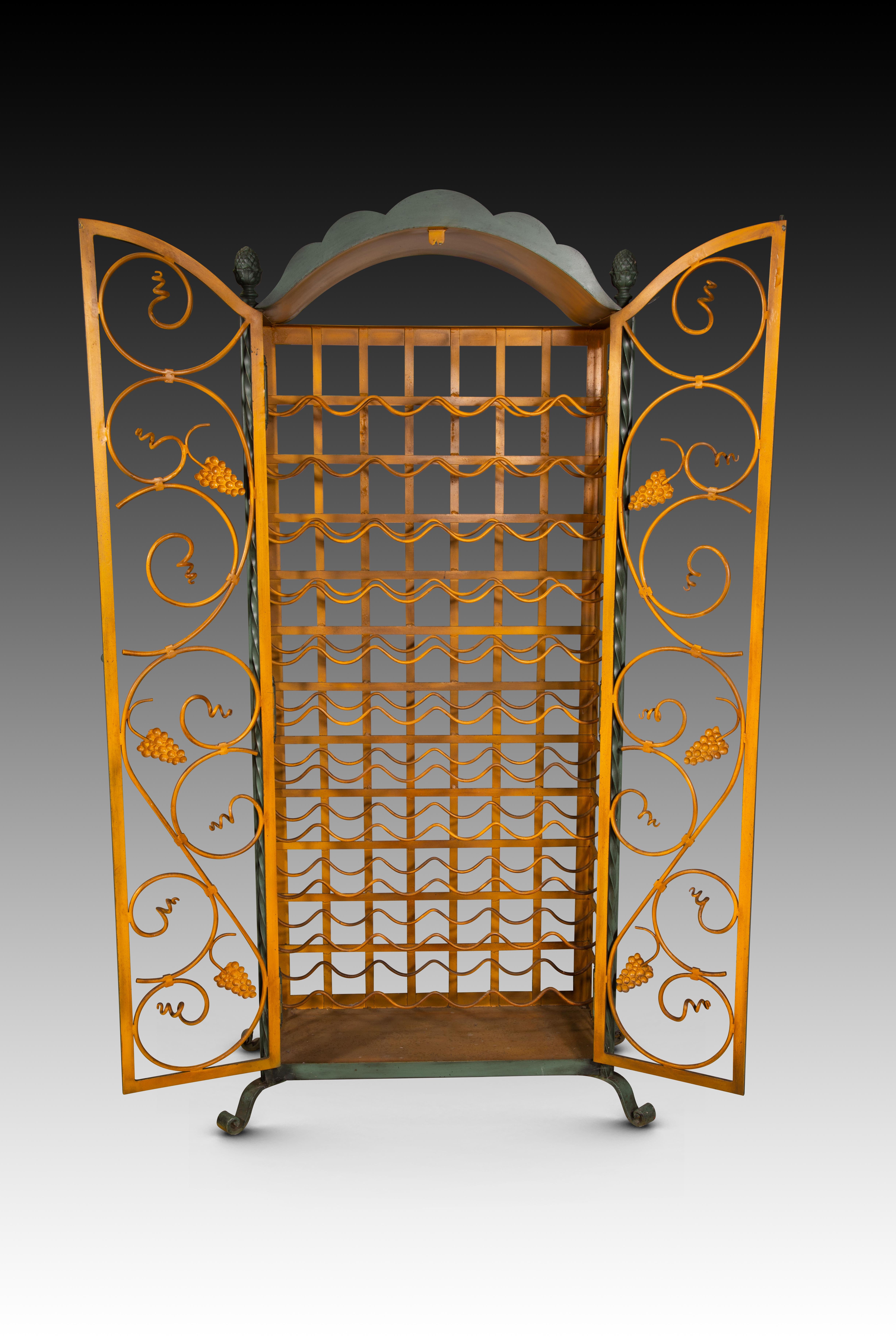  Bottle rack. Polychrome iron. 20th century. 
Tall cabinet with curved legs and double doors at the front, with iron shelves (double wires on each “shelf”) for storing bottles. It is decorated with curved rods accompanied by bunches of grapes at the