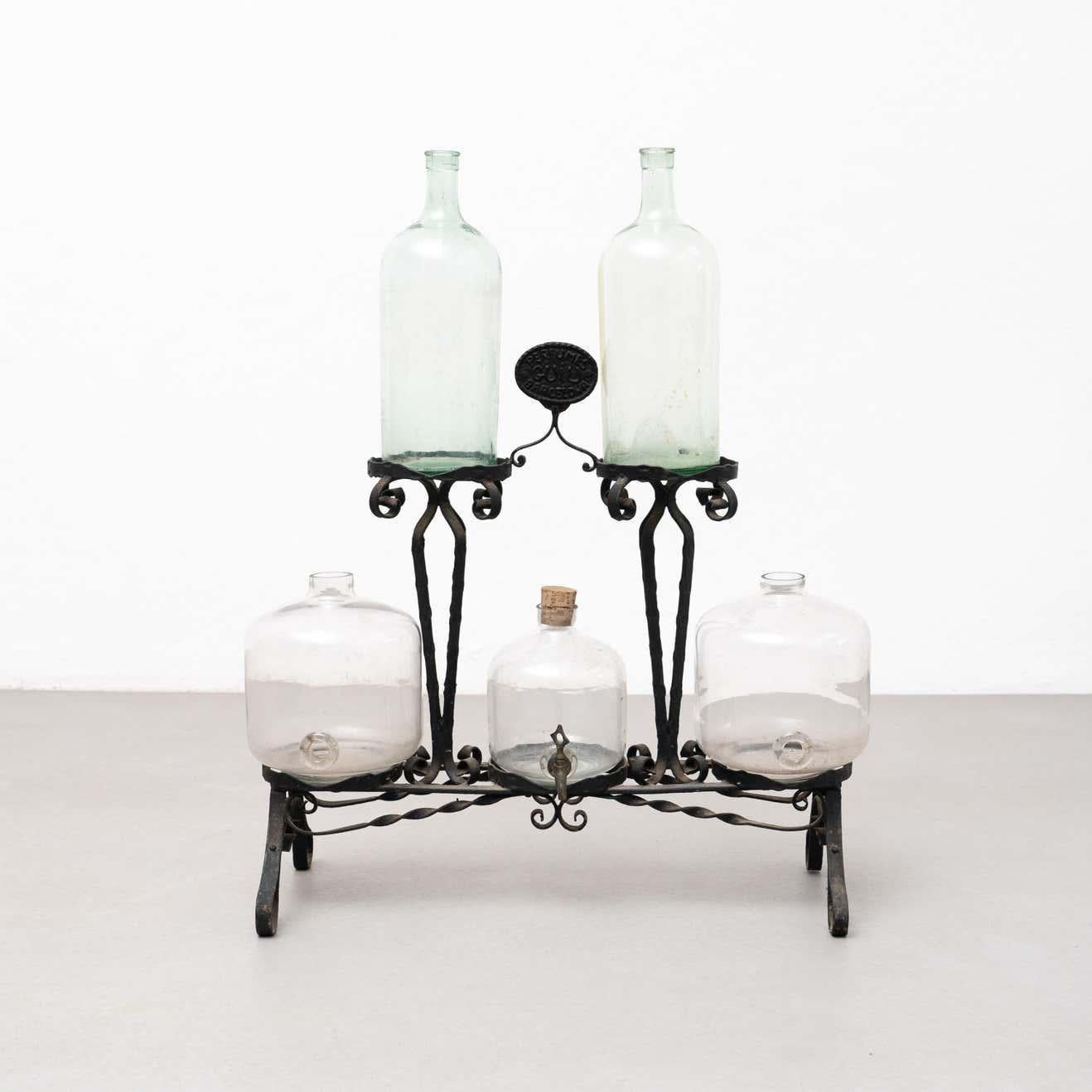 This antique display counter is a rare and beautiful piece of the Modernist movement in Barcelona, Spain. The ornate forged iron structure is stunning and perfectly complements the blown glass bottles, which have a gorgeous patina. One of the glass