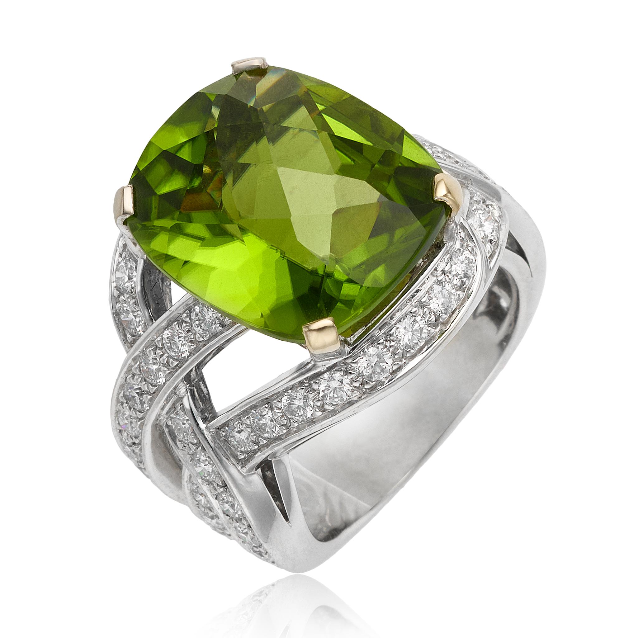 From designer Boucheron, 18 karat white gold peridot and diamond ring. This ring is crafted with a center 12.90 carat cushion cut peridot accented by round diamonds. These diamonds are pave set along the triple cross size 6.5 band. This ring is a