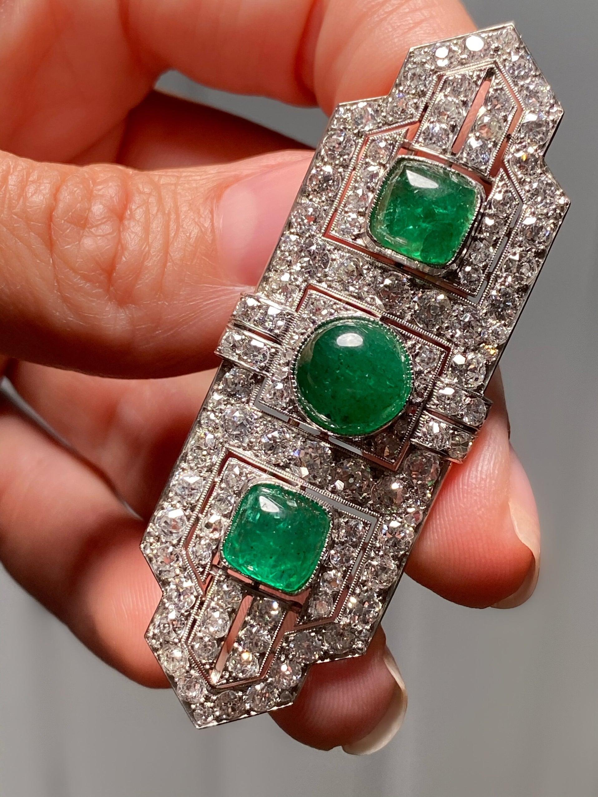 This sleek and sophisticated brooch was artfully designed and meticulously handcrafted by the esteemed French jeweler, Boucheron. Exquisite in every way, this linear brooch centers on a trio of richly saturated, crystalline green cabochon emeralds,