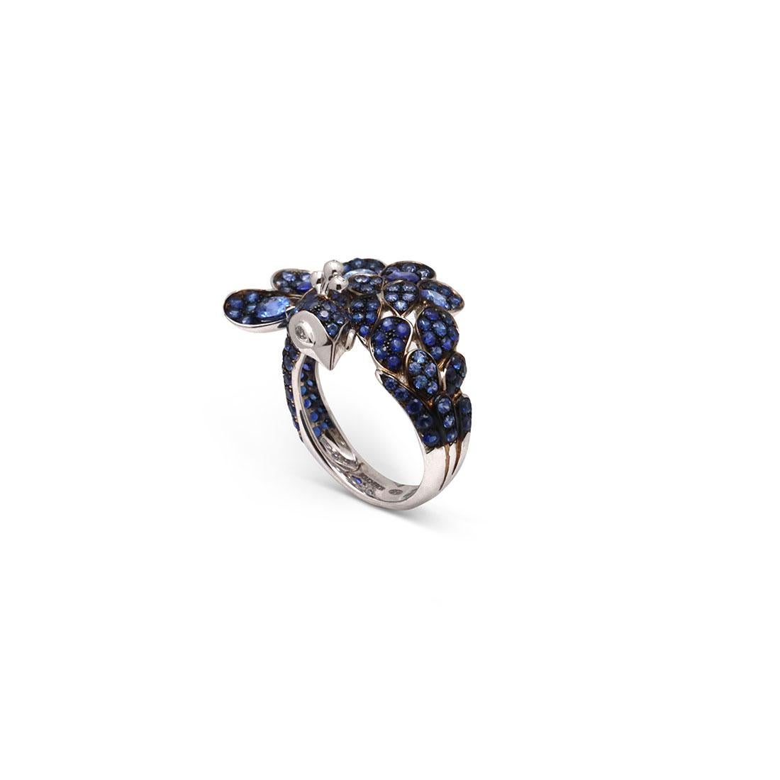 Authentic Boucheron Héra ring crafted in 18 karat white gold features a stunning peacock frame with pave round brilliant and pear-shaped blue sapphires. The eyes of the peacock are comprised of pear-shaped diamonds with an estimated .15 total carat