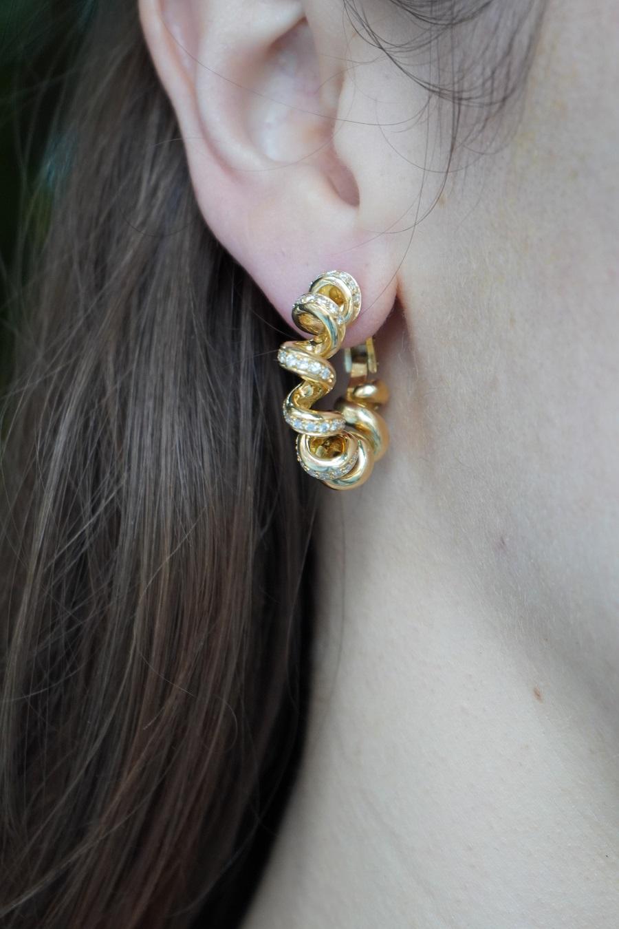A pair of Boucheron hoop earrings of swirl design, made of 18k gold, featuring  diamonds. 
A playful swirl motif twists and loops to form an open circle. Rounded and smooth curves create a dynamic sense of movement. Along select sections of the