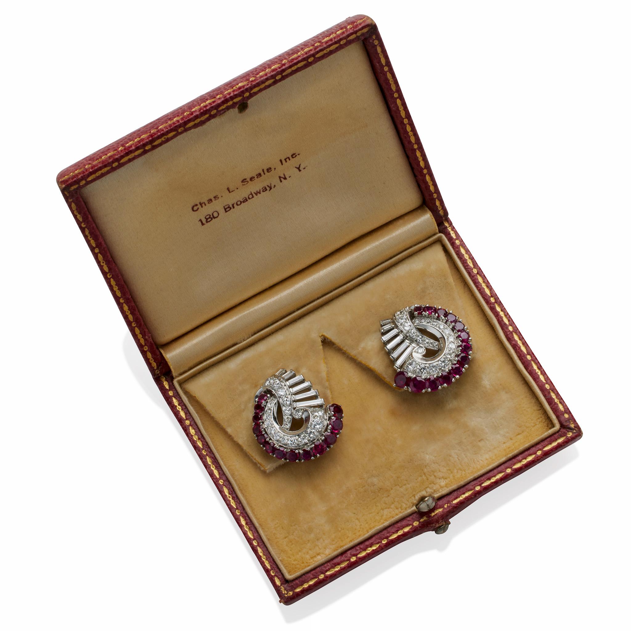 These diamond, ruby and platinum clip earrings date from the 1940s. Each clip earring is designed as an abstract swirl composed of round-cut rubies and diamonds, off-set by a plain polished scrolling element and graduating line of elongated