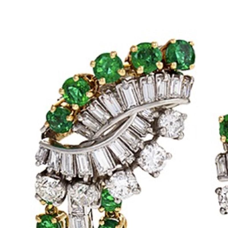A pair of French platinum and 18 karat gold earrings with emeralds and diamonds by Boucheron. The earrings feature a dynamic motif with platinum set baguette and round cut diamonds framed by round cut emeralds set in gold. The earrings' drop