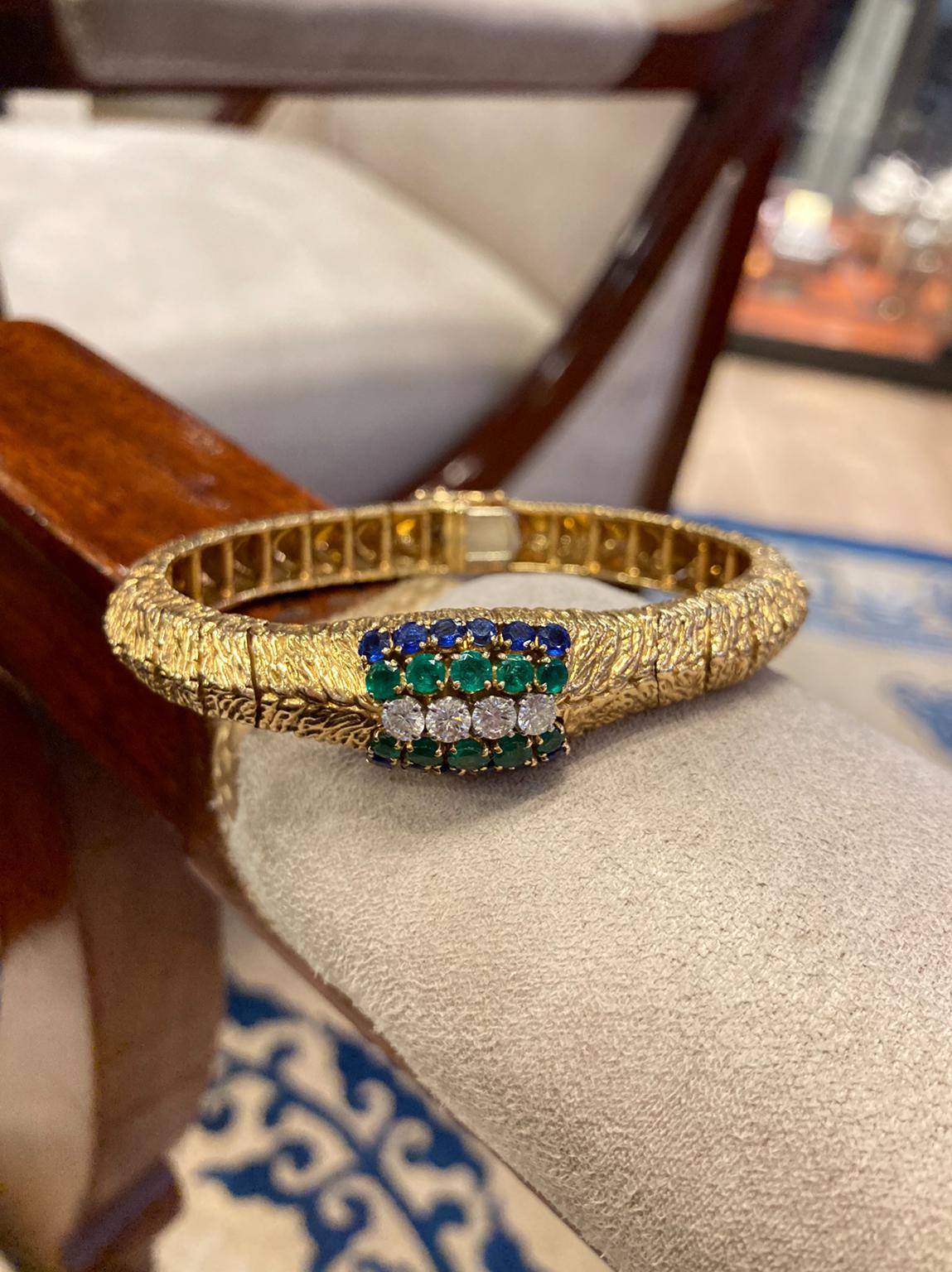 A retro Boucheron Paris 18 karat yellow gold mystery watch-bracelet with brilliant cut sapphires, emeralds, and 0.70 carats of diamonds. Weighs 54.6 grams. Made in France, circa 1940.