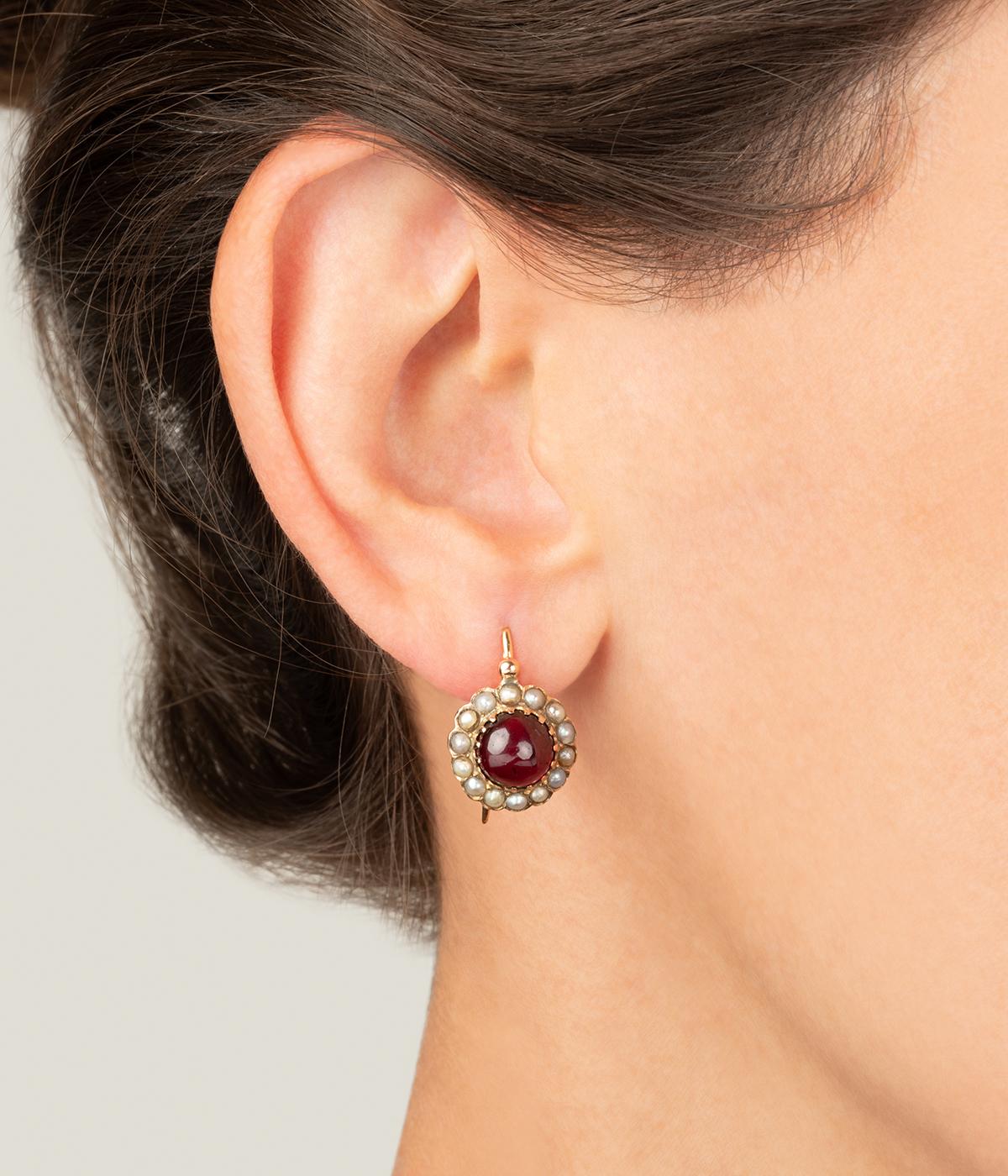 Boucles d'oreilles dormeuses anciennes en or jaune 18 carats (750 millièmes) de la fin du 19ème siècle, serties d'un cabochon de grenat (env. 3 carats chacun) dans un entourage de perles fines.

Poids total du bijou : 5,64 g environ.
Hauteur 2,2 x