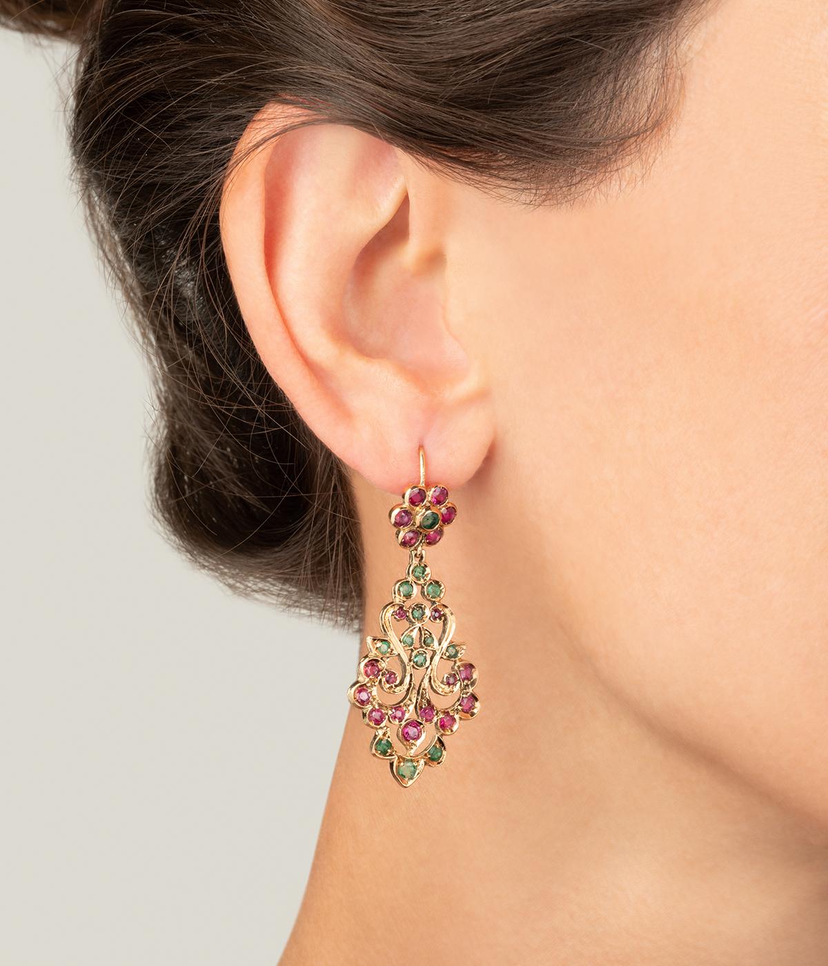 Pendants d'oreilles vintage en or 18 carats (750 millièmes). Ajourés, ils sont à décor de fleurs et d'arabesques serties de rubis et d'émeraudes.

Poids total du bijou : 8,4 g environ.
Hauteur 5,1 x Largeur 2 cm.
Poinçon tête d'aigle.