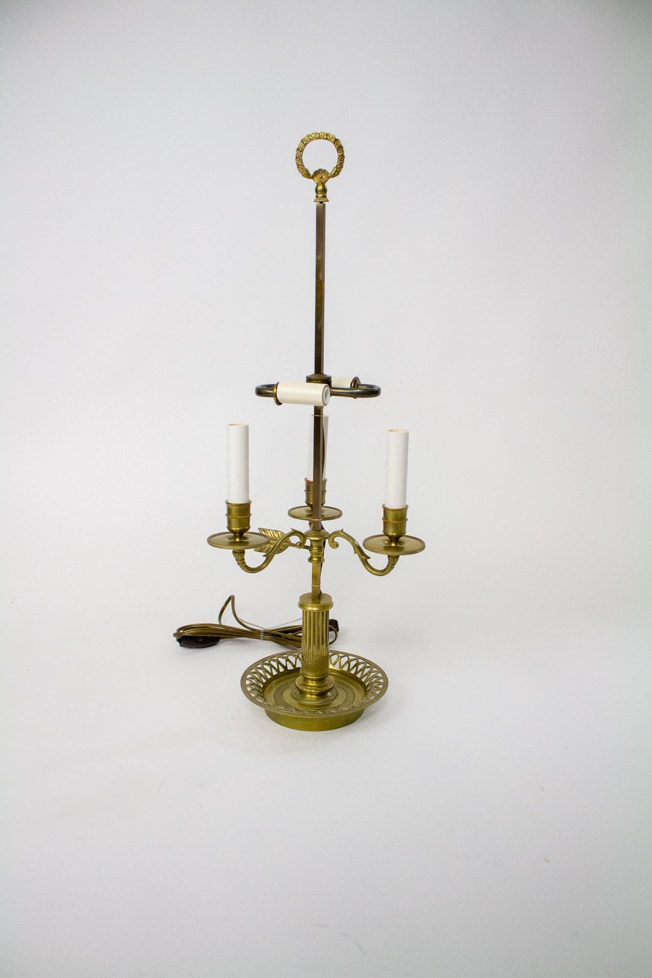 Bouillotte lamp in cast brass. The three arms That extend from the stem are for candle. There is a hidden two light cluster that takes candelabra bulbs. 60 Watt max per socket. Bottom tray is round with a decorative edging. The shade is a forest