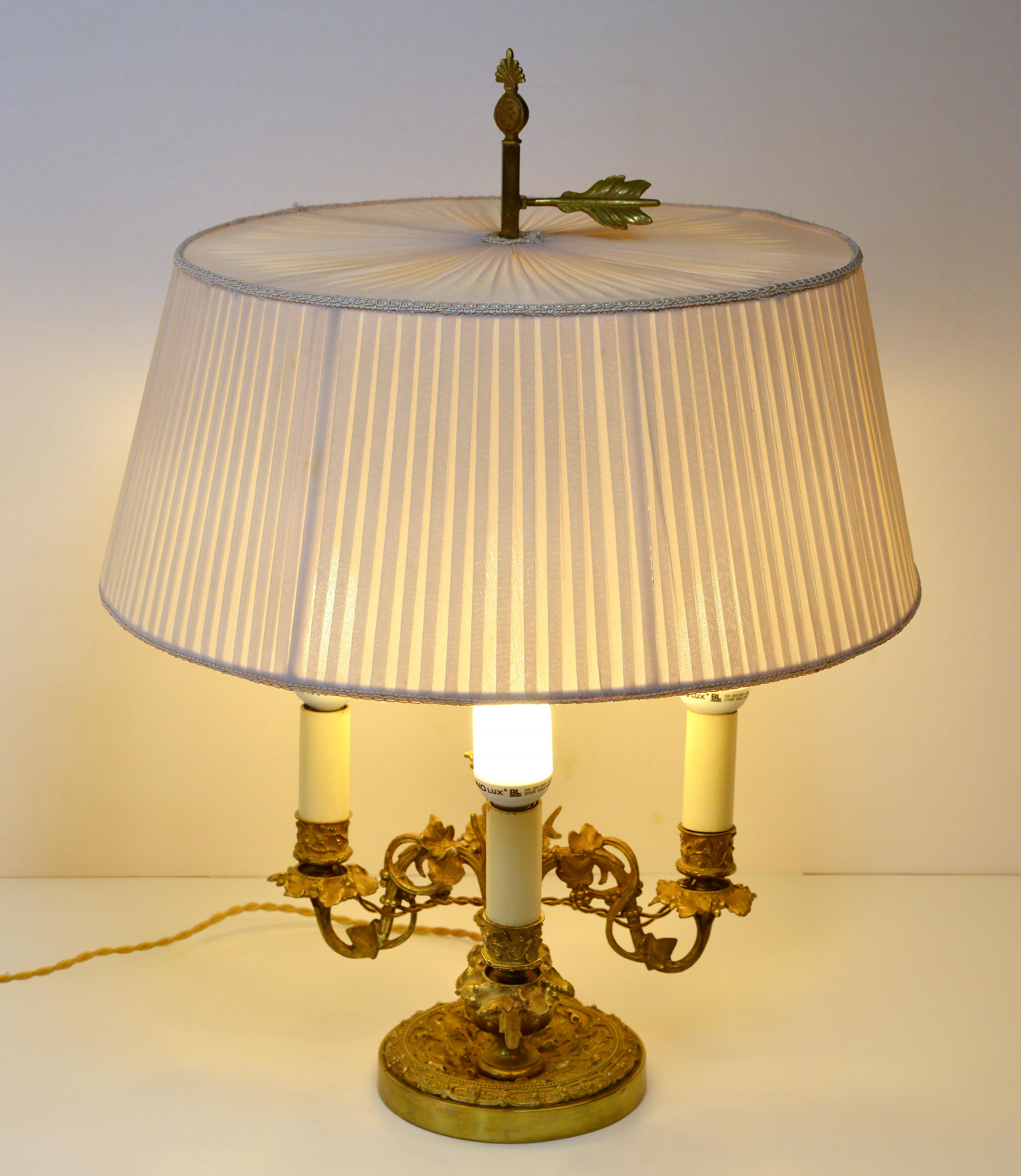 Stilvolle antike Bouillotte-Lampe. Quadratischer Fuß mit vier Kerzenhaltern mit Flora-Motiv und verstellbarem Stoffschirm  mit Fixierbolzen in Form einer Pfeilfeder. Der Lampenschirm wurde höchstwahrscheinlich ersetzt, als die Lampe elektrifiziert