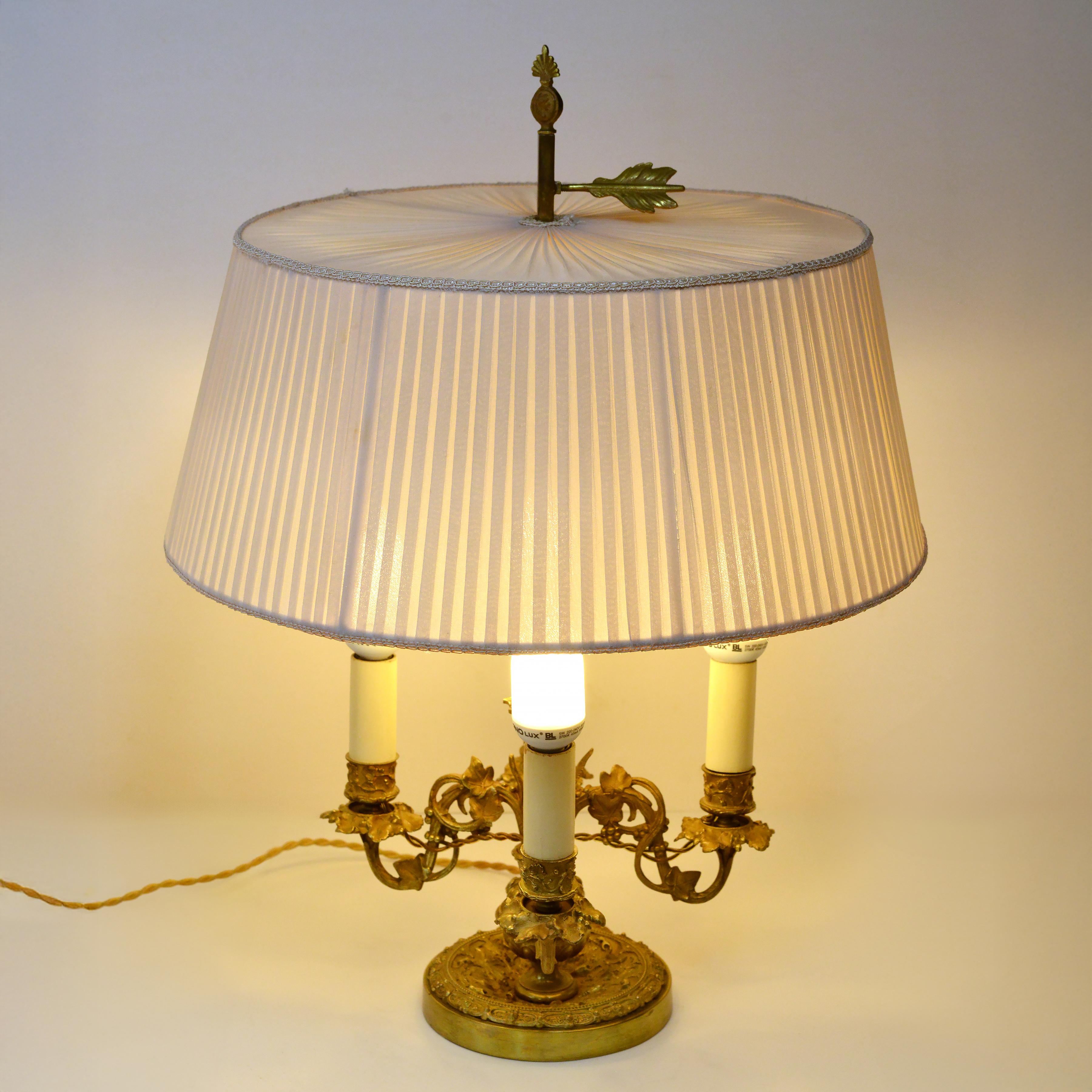 Élégante lampe Bouillotte ancienne. Pied carré avec quatre bougeoirs en motif flore et abat-jour réglable en tissu.  avec boulon de fixation en forme de plume de flèche. L'abat-jour a probablement été remplacé lorsque la lampe a été électrifiée pour