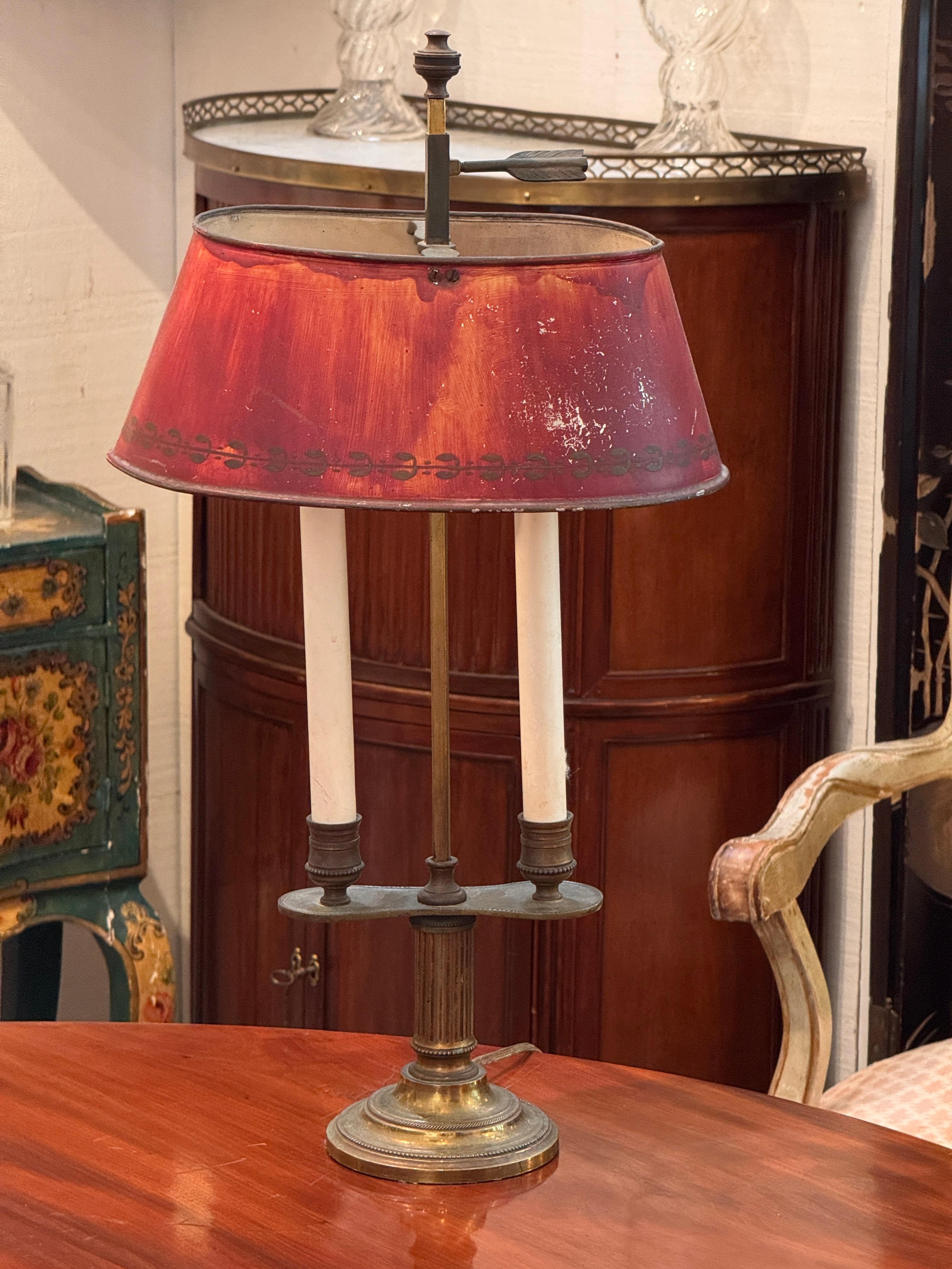 This bouillotte lamp features a gilt and patinated brass column base with fluted detail and a stepped circular foot edged in fine beaded decoration. It has two candlestick-style arms rising from an oval platform, with turned nozzles accented by