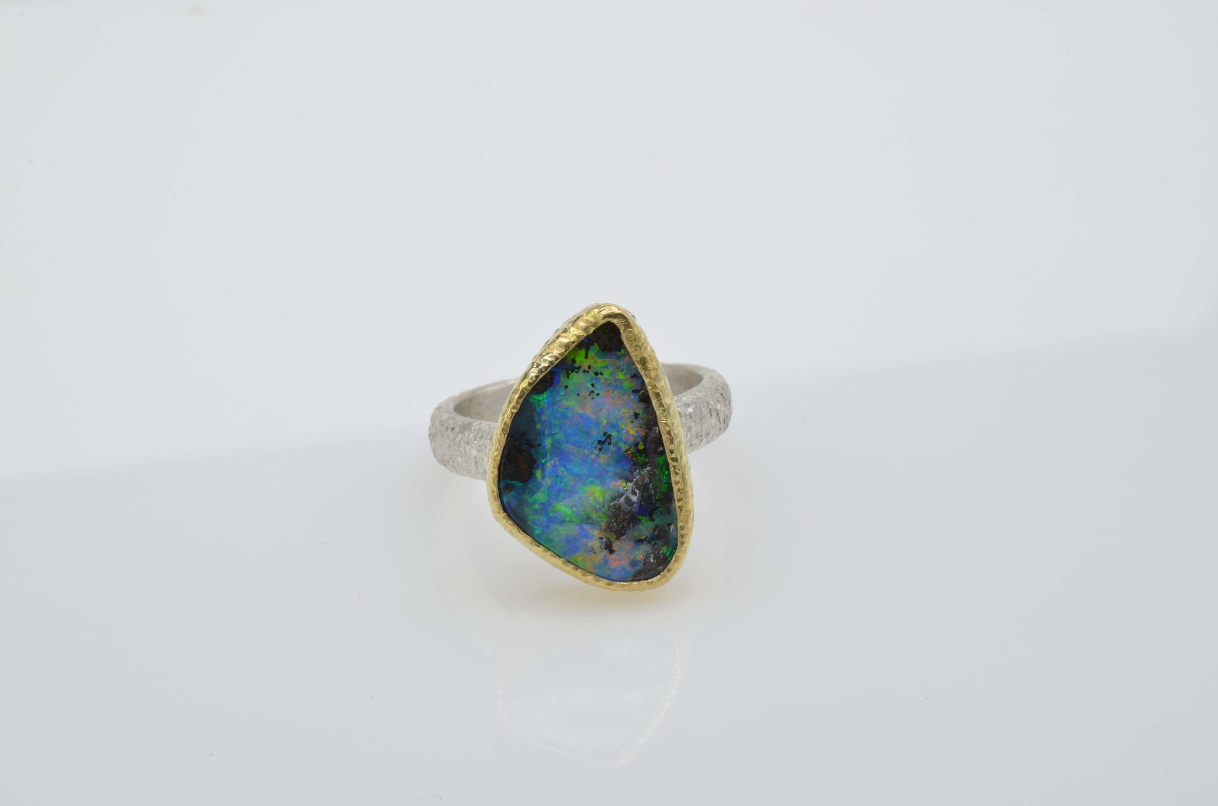 This magnificent boulder opal has incredible fire and color. The 14k gold bezel beautifully compliments the color of the stone.  The band is sterling silver and both have a handcrafted hammered texture. The ring size is a 7 and can be sized to fit