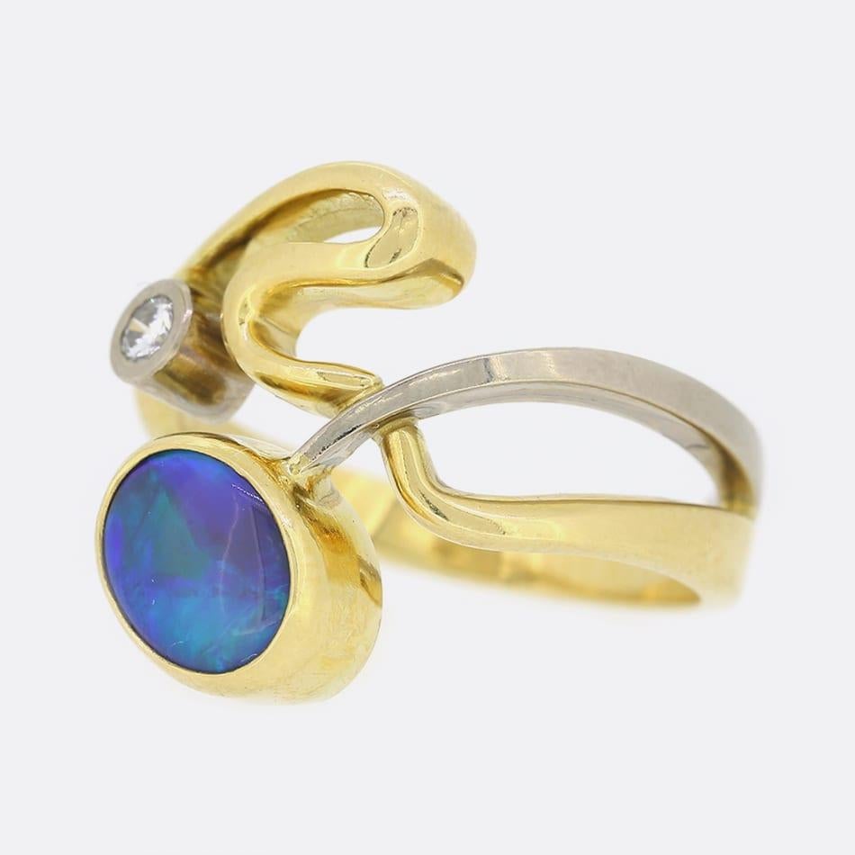 Si tratta di un anello astratto con opale boulder e diamanti in oro giallo 18ct. L'opale principale è incastonato in un castone, ha un taglio ovale e presenta un meraviglioso gioco di colori. Questa pietra principale è completata da un singolo