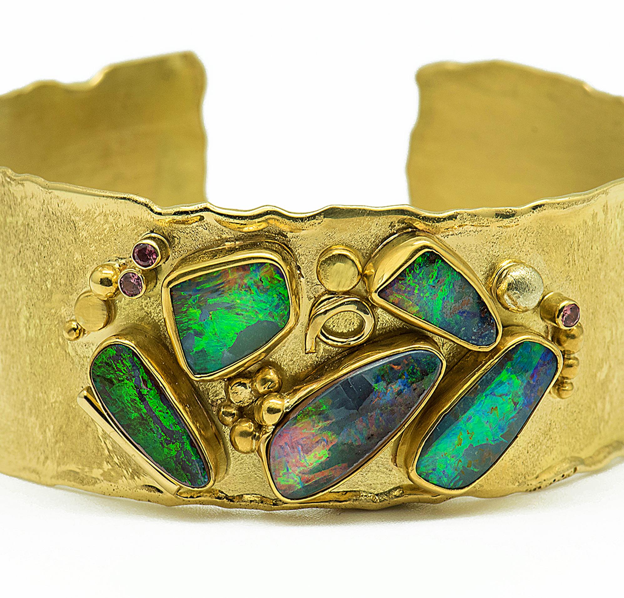 Boulder opal cuff bracelet with 5 boulder opals in the green, blues and some flashes of red.  18k gold arabesque design elements sprinkle the surface of a 18k gold cuff;  accented with sapphire and garnet.  The cuff is 1.0