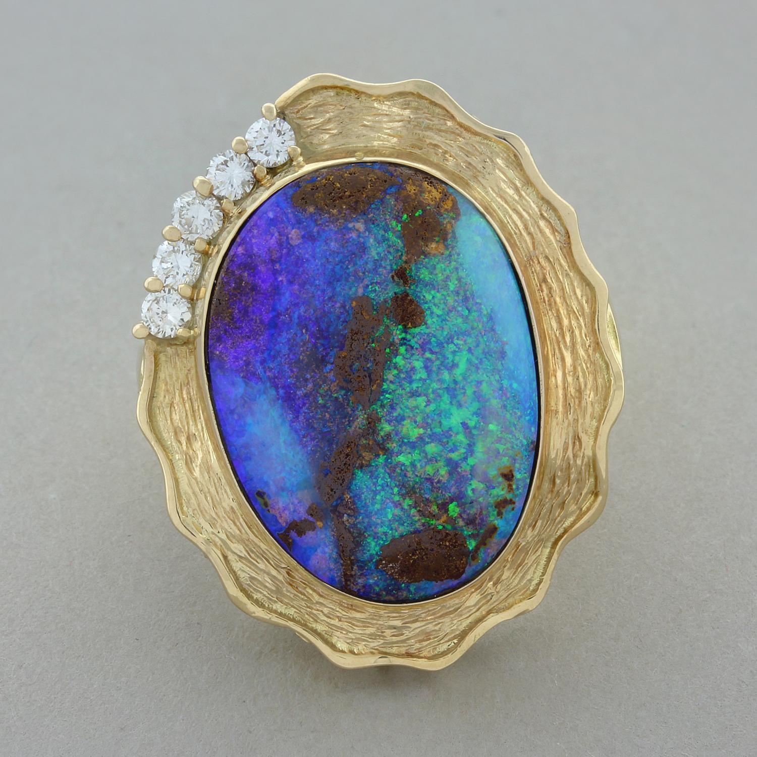 A magnificent ring featuring a 14.15 carat boulder opal bezel with exceptional play of color. The opal is accented by 5 round brilliant cut diamonds totaling 0.32 carats. The ring is hand fabricated in 18K yellow gold with a textured finish around