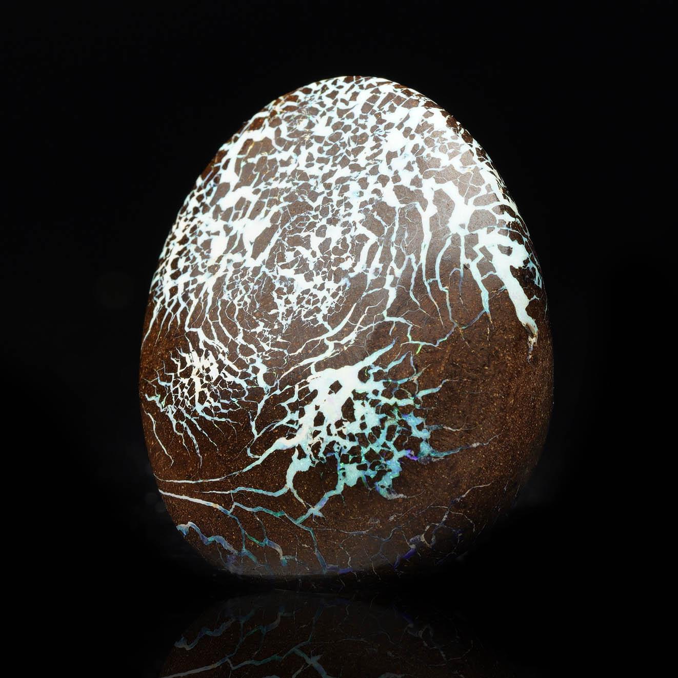 Este exquisito Ópalo Boulder de Australia presenta un vibrante juego de colores, con azules eléctricos, naranjas ardientes y verdes profundos que brillan sobre su matriz natural de piedra de hierro. La superficie pulida del ópalo resalta sus