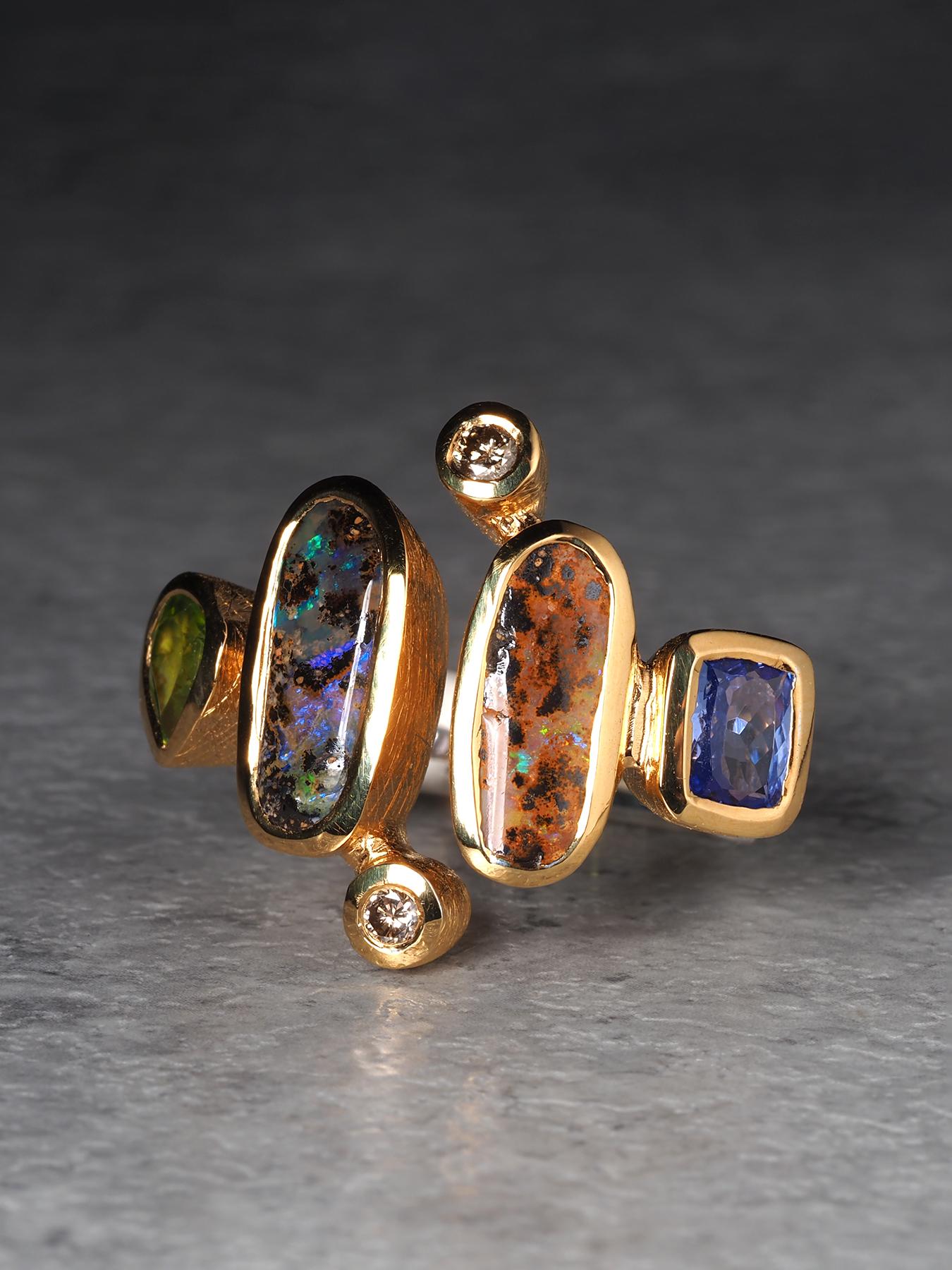 Ein außergewöhnlicher Ring, der die einzigartige Schönheit der australischen Boulder-Opale, gepaart mit Peridot, Tansanit und Diamanten, zur Geltung bringt. Die länglichen Cabochon-Opale zeigen ein fesselndes Farbenspiel - eine erdbraune Matrix