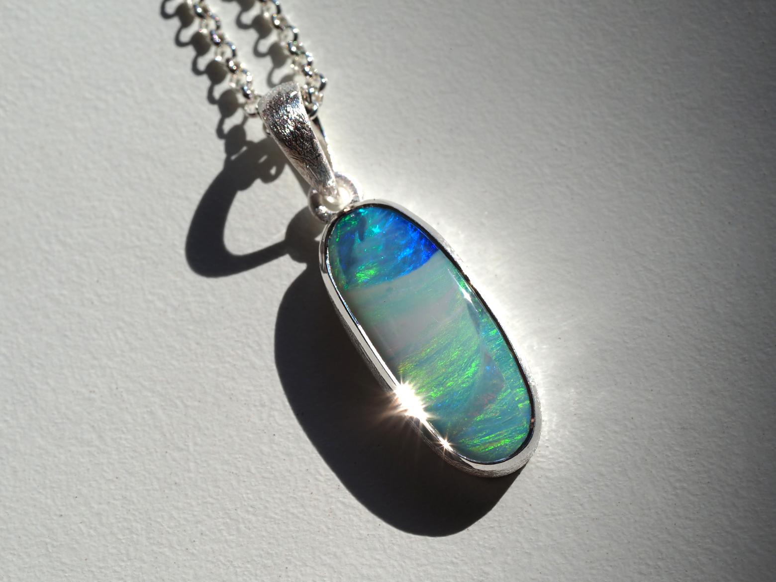Questo elegante ciondolo in argento è incentrato su un'opale Boulder australiana di raffinata bellezza. Con dimensioni di 8 x 20 mm e un peso di 5,20 carati, l'opale mostra un vivido gioco di colori naturali, che si spostano con la luce per rivelare