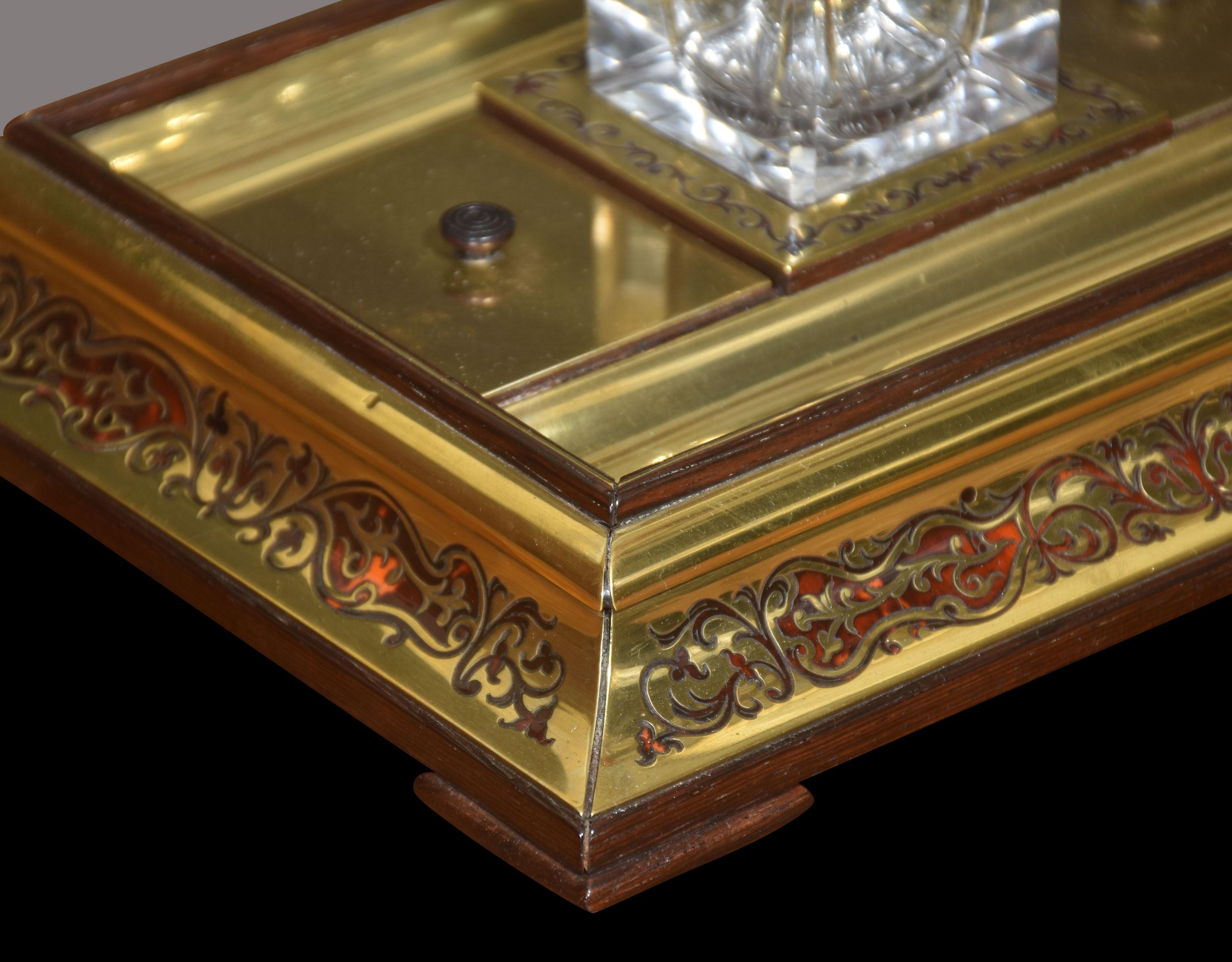 Boulle brass inkstand, supporting the original clear cut glass inkwell with hinged cover. Having pen tray at either side. Raised up on a rectangular base.
Dimensions
Height 5 Inches
Width 9.5 Inches
Depth 8 Inches