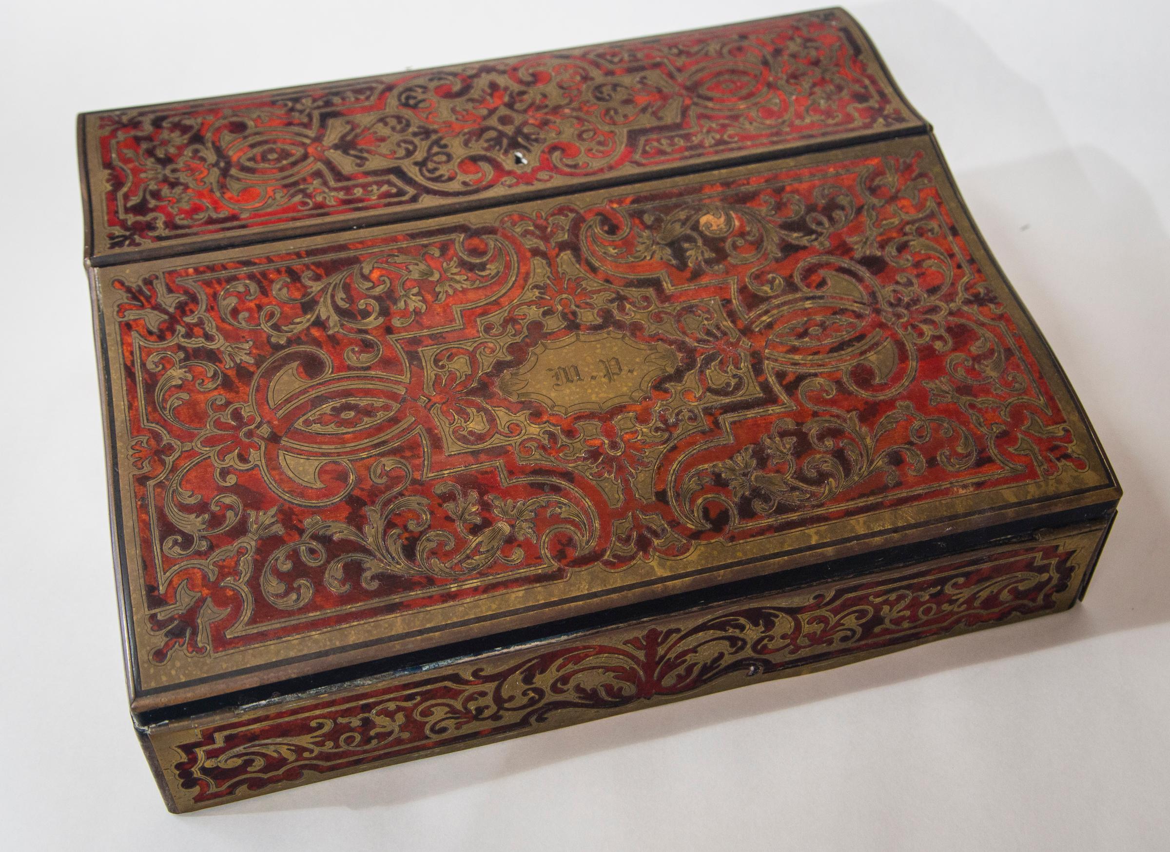 Dating from the era of Napoleon III. If tortoiseshell with inlays of brass scrolling.
The top opens for pens and ink bottles
The writing surface is a double fold out, now covered in blue velvet. The lower writing surface lifts up for storage of