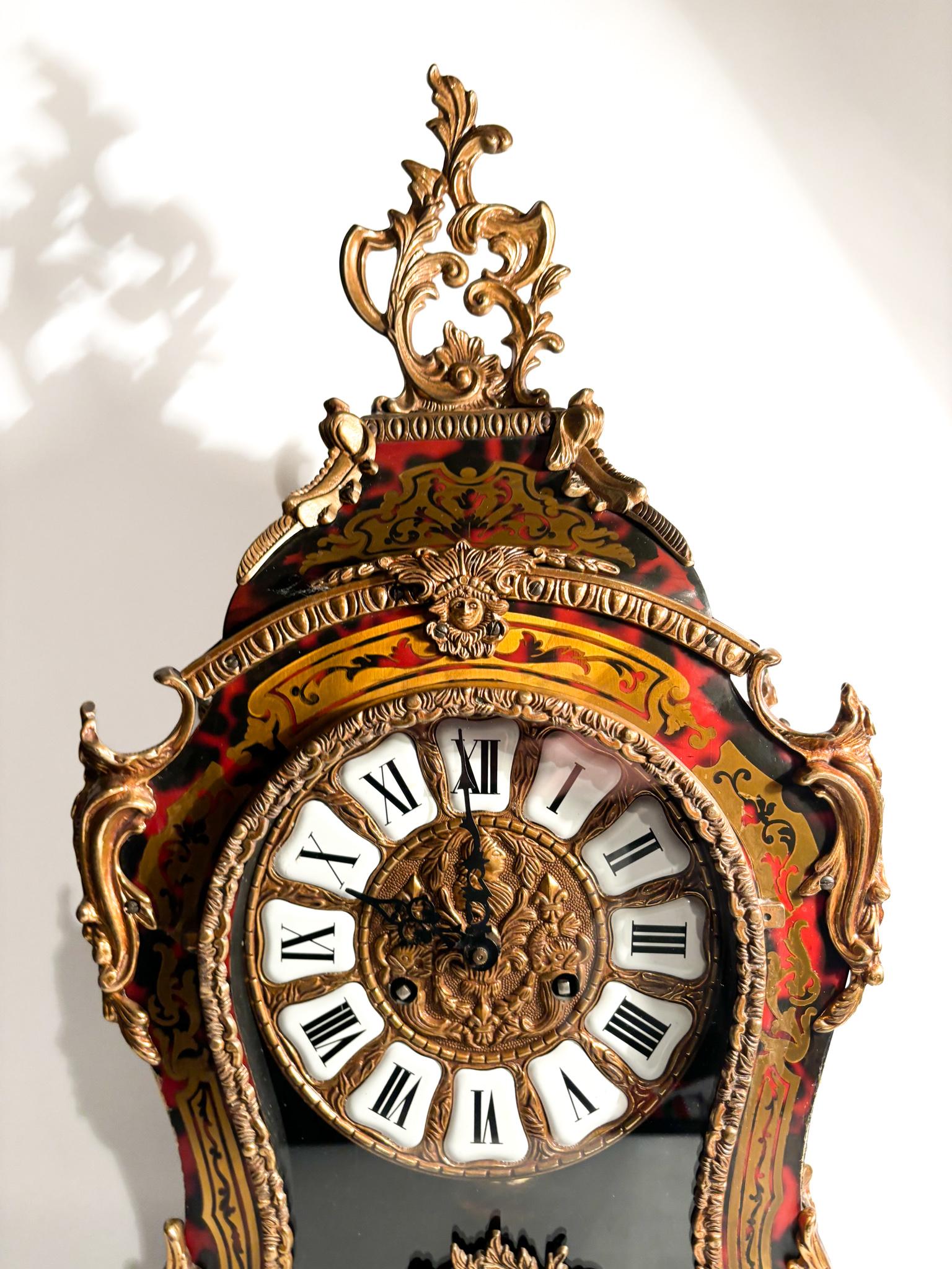 Boulle Table Clock, with red background and brass inlays, brass dial with white enamel cartouches and black Roman numerals, crowned with rocailles and pendulum movement. 

Ø 31.5 cm Ø 15 cm h 58 cm

A Boulle clock is a type of decorative clock
