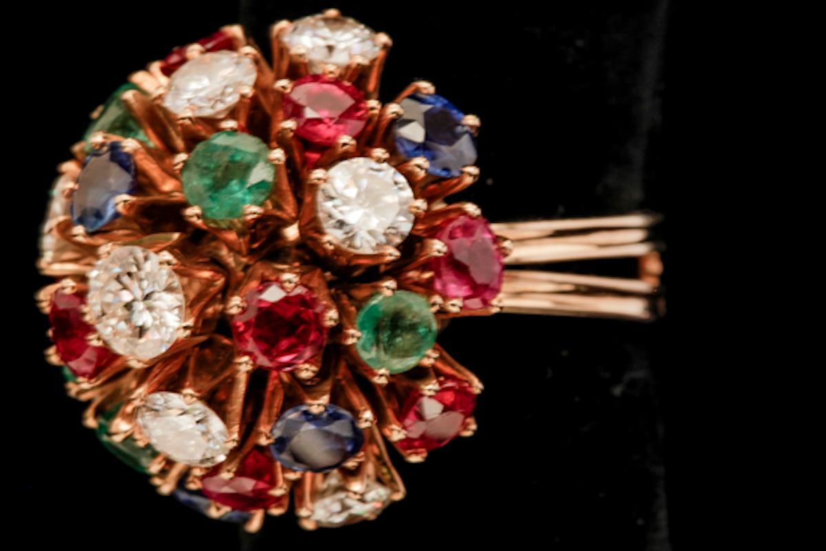 A lady's 18k yellow gold, diamond, ruby, emerald and sapphire ring. This Bouquet style ring has 25 various stones weighing approximately 7.08 carats set into five prong heads. There are (7) round brilliant cut diamonds with an estimated total weight