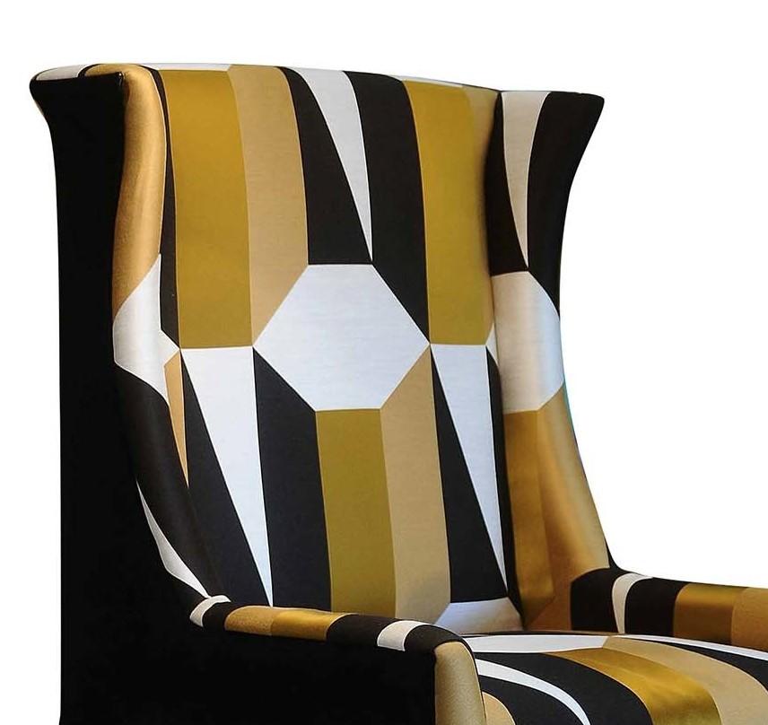 This stunning armchair is a bold and sophisticated addition to a modern living room, study, or entryway. Its beechwood structure is enriched with a finish in bronze leaf visible on the legs for a striking look. The classic wing chair design of the