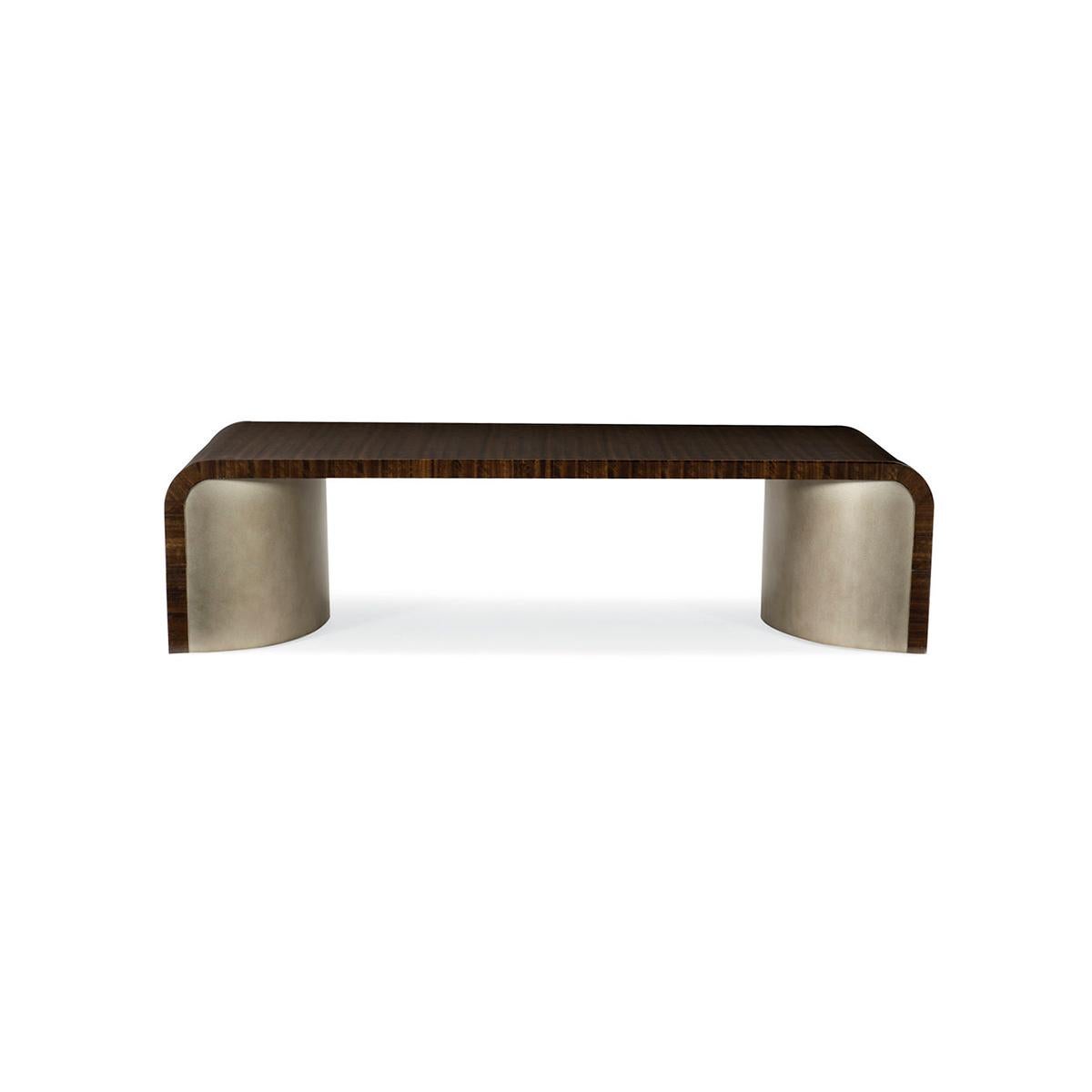 Fumed figured eucalyptus wood, finished to a high sheen in luscious Aged Bourbon, wraps the top of this rectangular table that is void of sharp angles. Two large, half-moon-shaped pedestals support the piece and are covered in Smoked Bronze. The