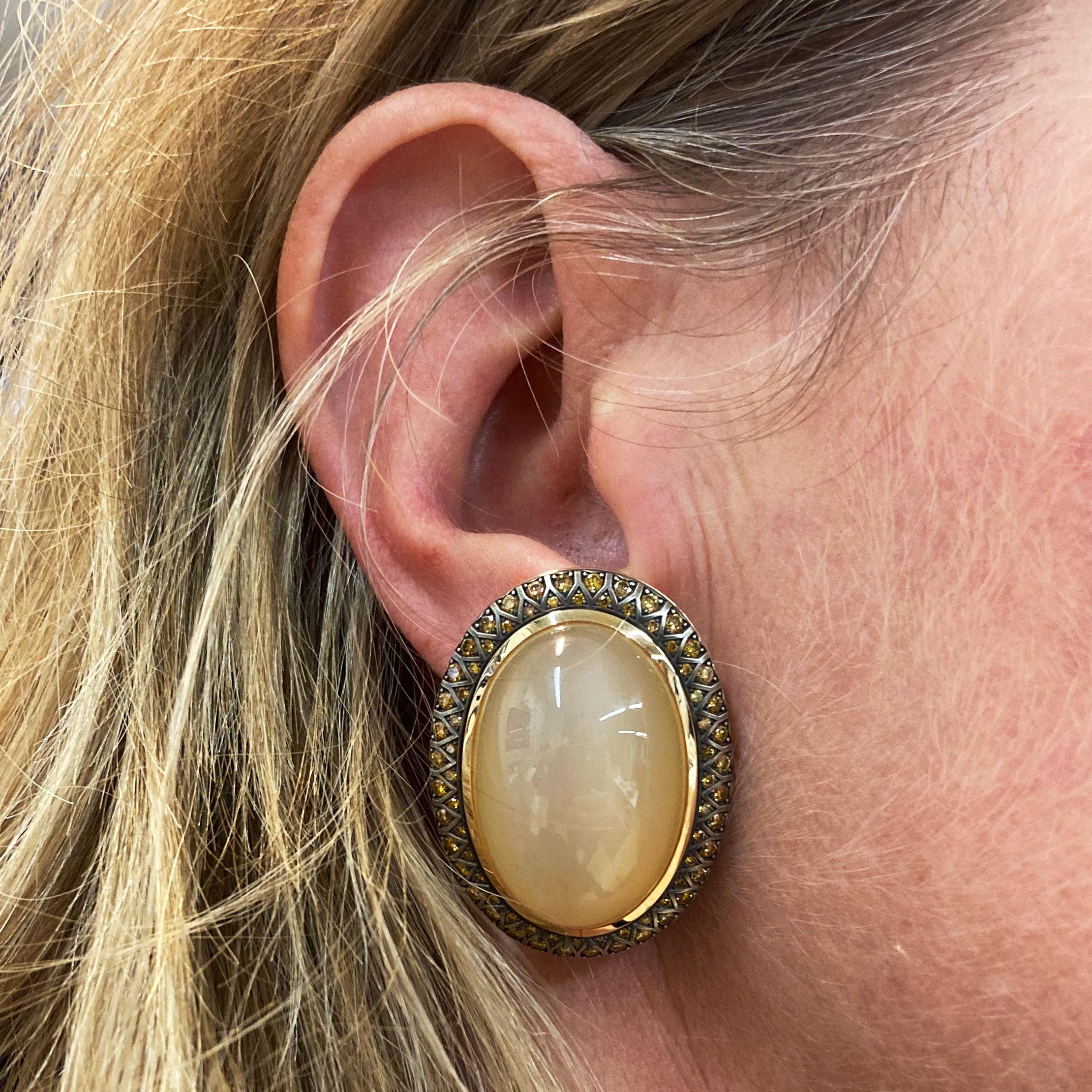 These Bouton Clip-on Earrings  are made in Sterling Silver and rose Gold 18 Kt . A blackened surface shows 2 honey colored Moonston cabochons  of a total weight of  93.72 ct  with a spectacular play of light.  144 Diamonds natural fancy deep yellow