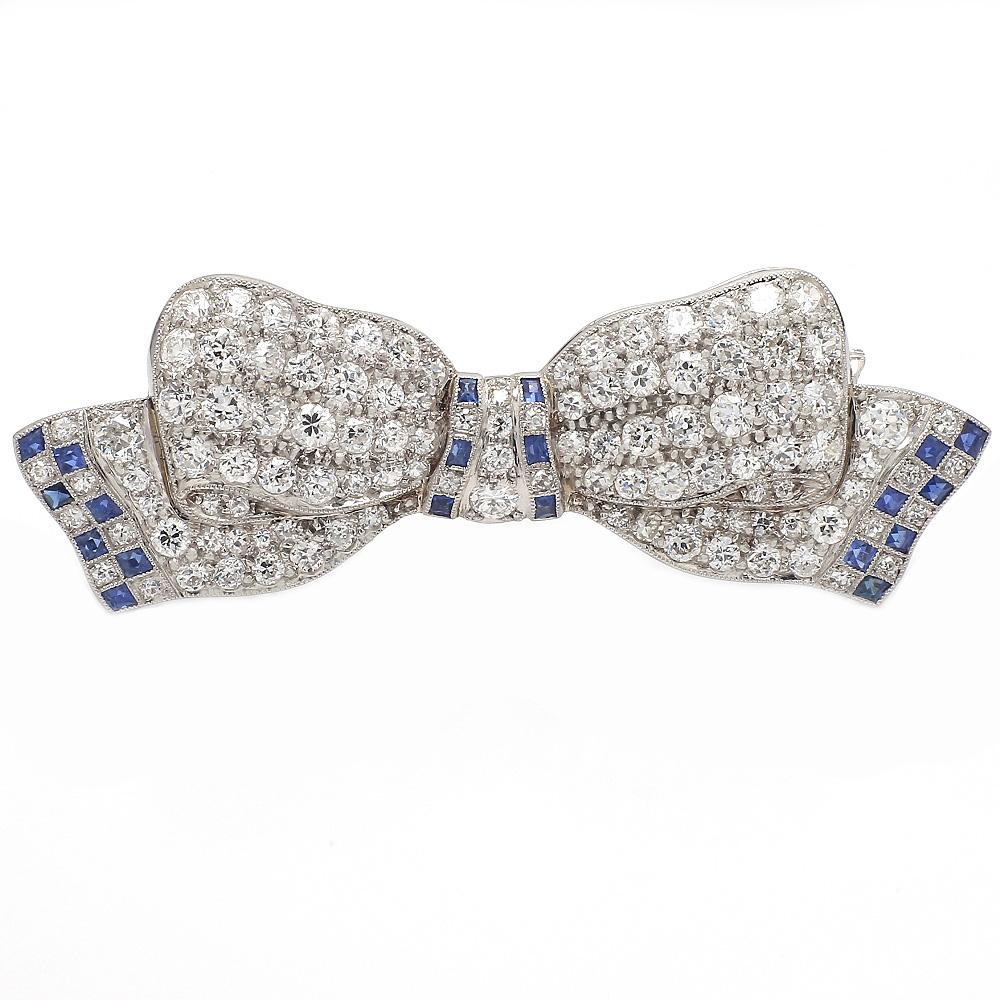 Platinum Bow Brooch with Diamonds and Sapphires

This elegant brooch showcases a stunning array of white diamonds, each cut in a classic French style, creating a dazzling display. The diamonds are complemented by vibrant blue sapphires, adding a