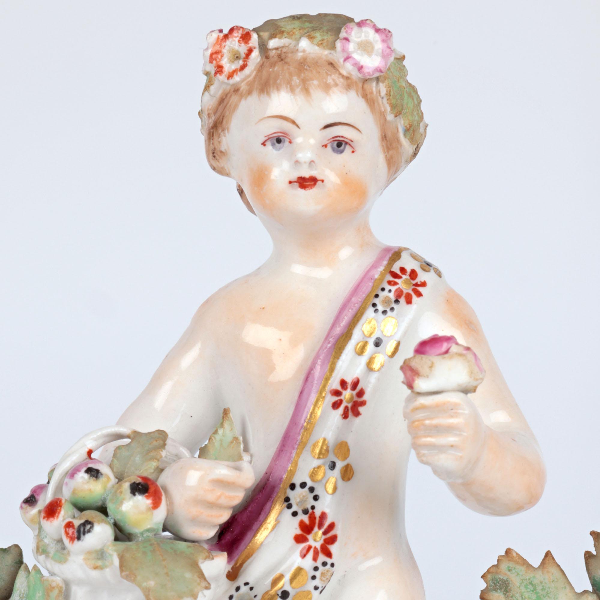 A scarce antique English porcelain figure of a Putto holding a basket of flowers by the renowned Staffordshire factory Bow and dating from around 1760. The Putto stands raised on an open scroll work base on five legs with the base adorned with