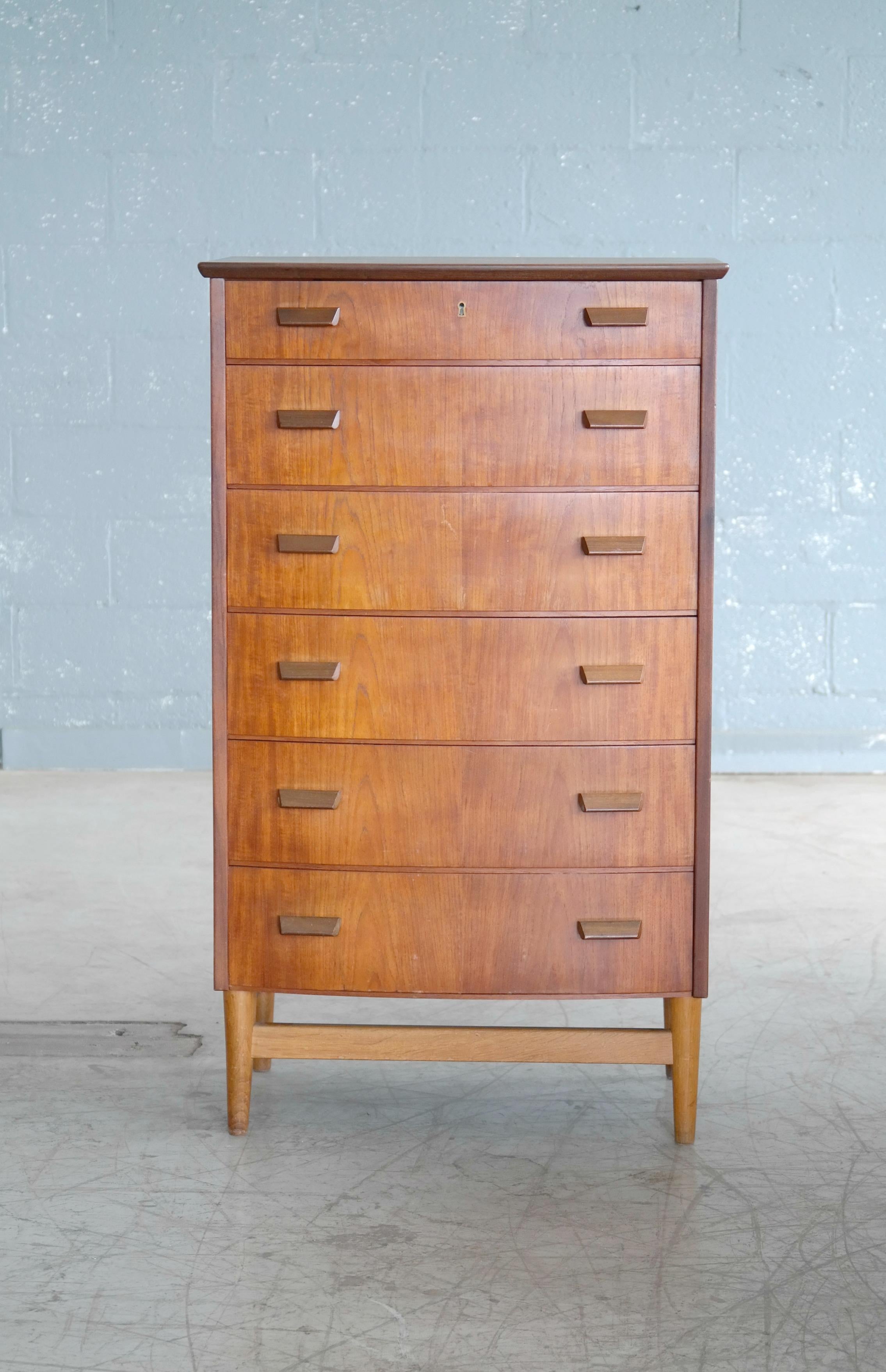 Beautiful bow-front Danish teak high-boy dresser or chest of drawers in the style of Borge Mogensen. Highest build quality teak veneer backed by solid ply. Beautifully figure grain and color. Carved pulls in solid teak all raised on a contrasting