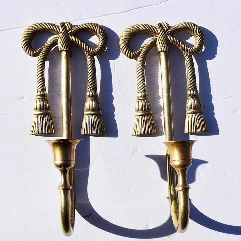 A beautiful pair of tall brass trompe l'oeil one arm candle sconces. This pair holds one candle per sconce. And feature a bow and ribbon motif design. At the top, a ribbon is tied into a knotted bow which is created out of beautiful solid brass. The