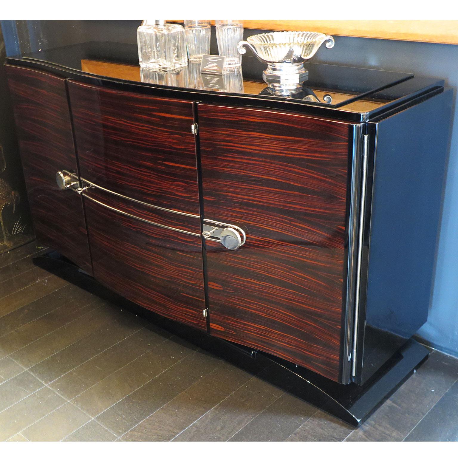 Smaller, elegant Art Deco sideboard with three Macassar ebony front doors. The bowed rectangular frame is entirely in black lacquer along with the base. The top has a thin black glass top. Original polished nickel hardware adorns the front doors.