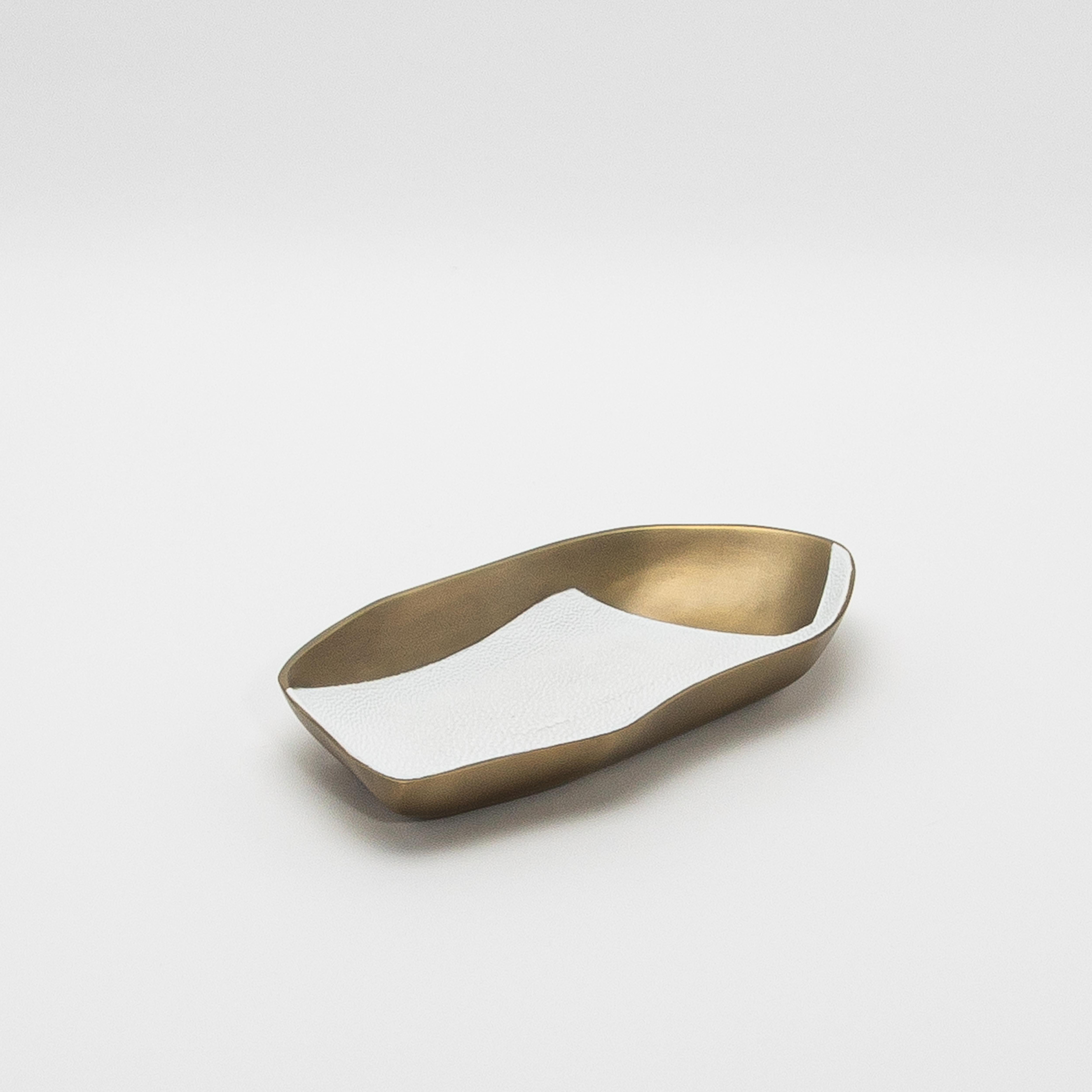 El cuenco Chital de KIFU Paris es una asombrosa combinación de forma y textura, fabricado en latón patinado en bronce y exquisitamente detallado con una incrustación de piel de zapa blanca en contraste. Su forma orgánica, con bordes ondulados, evoca